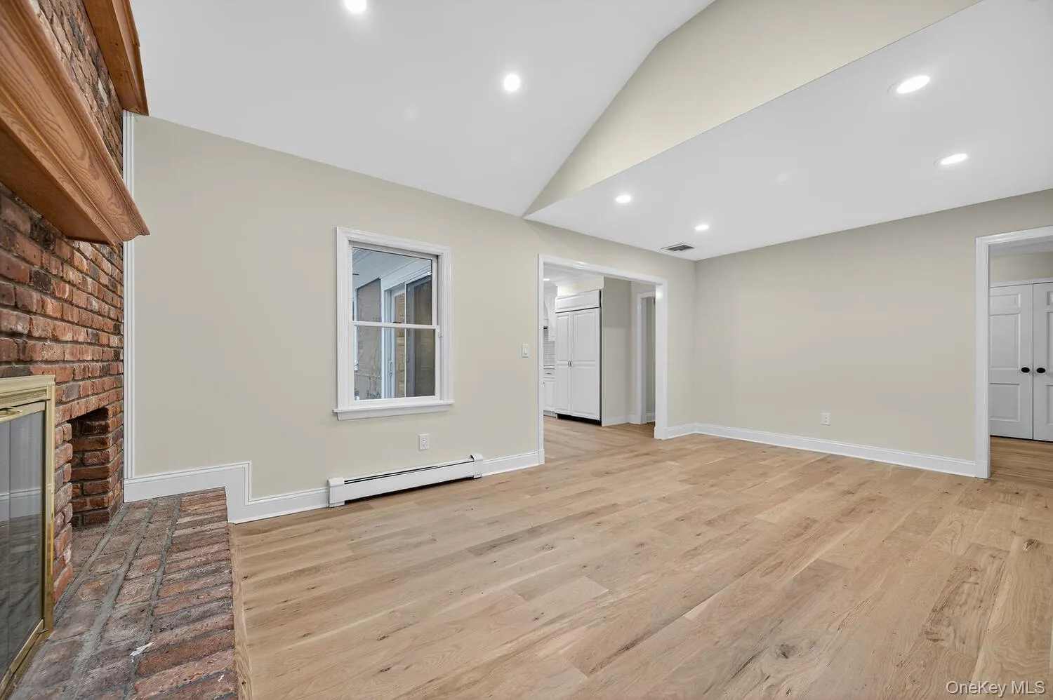 den featuring light wood-type flooring, lofted ceiling, a baseboard heating unit, a brick fireplace, and recessed lighting den featuring light wood-type flooring, lofted ceiling, a baseboard heating unit, a brick fireplace, and recessed lighting
