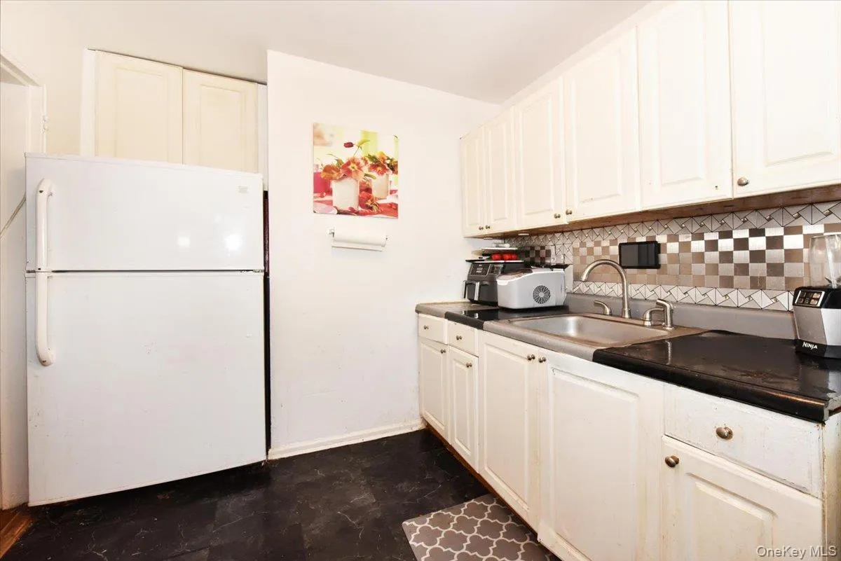 Kitchen featuring dark countertops, freestanding refrigerator, tasteful backsplash, and white cabinets Kitchen featuring dark countertops, freestanding refrigerator, tasteful backsplash, and white cabinets