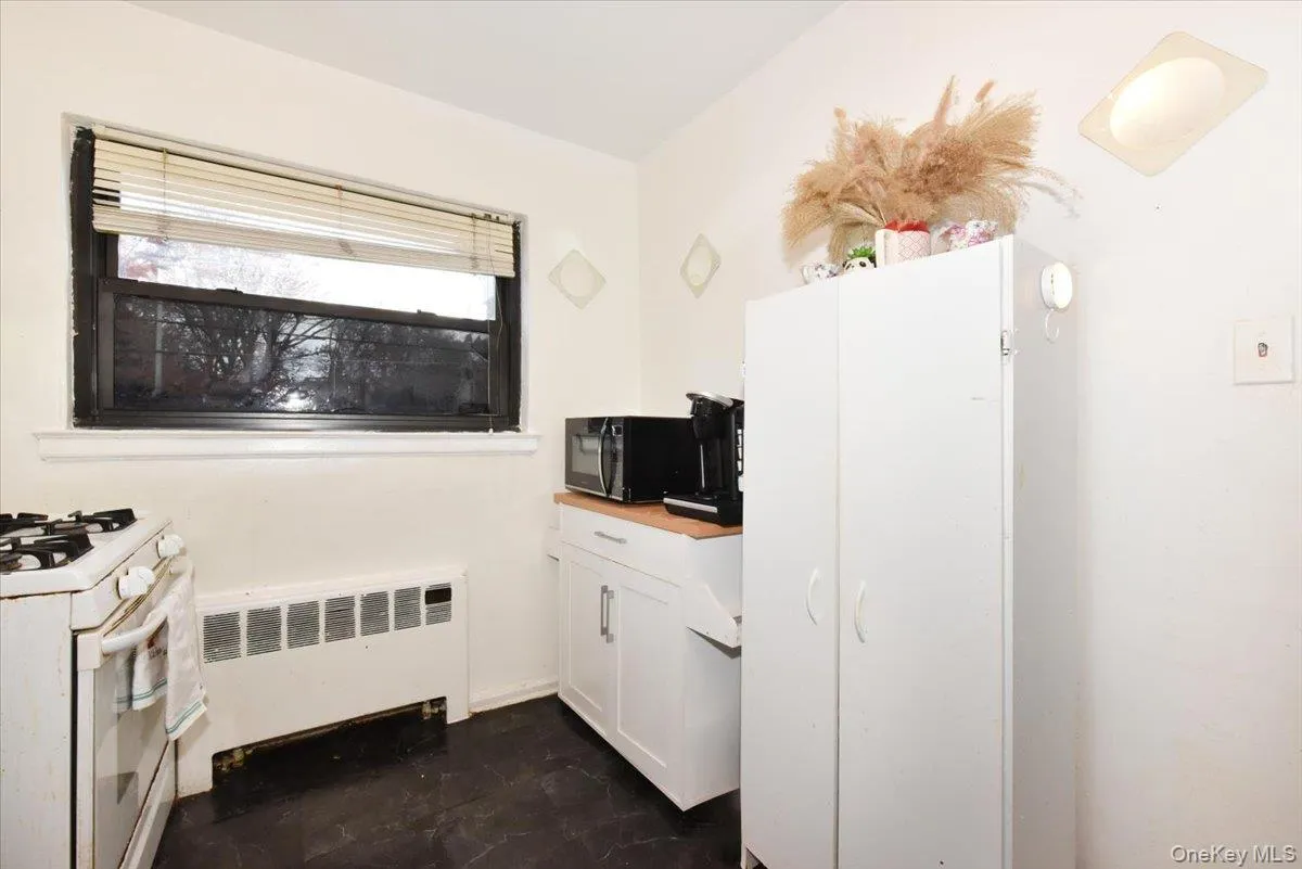 Kitchen with white cabinetry, radiator heating unit, black microwave, butcher block countertops, and gas range gas stove Kitchen with white cabinetry, radiator heating unit, black microwave, butcher block countertops, and gas range gas stove