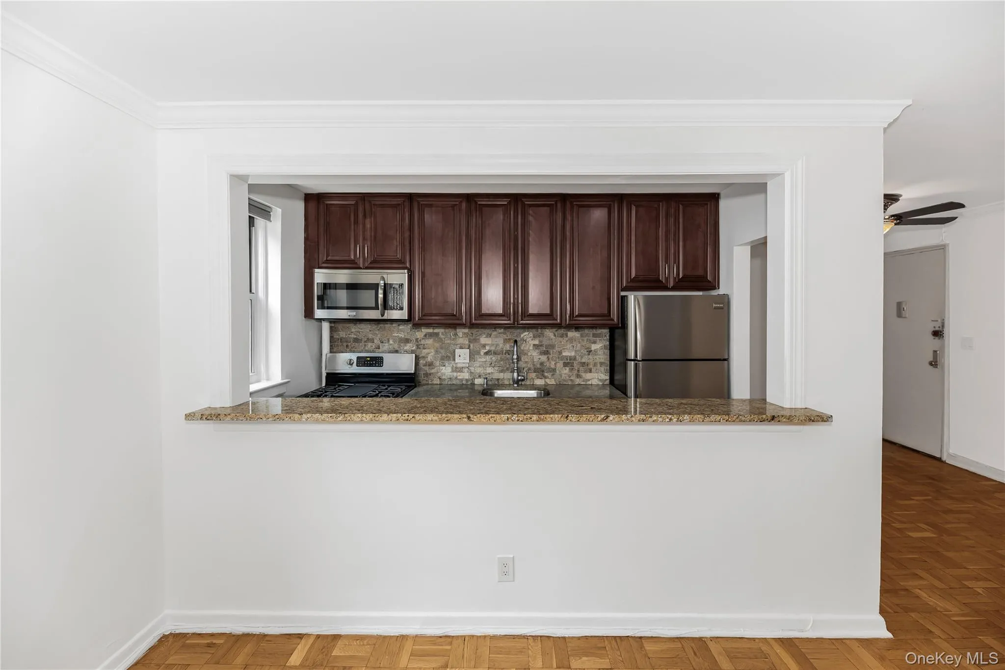Living room looking into kitchen with appliances with stainless steel finishes, crown molding, tasteful backsplash, dark stone counters, and a ceiling fan Living room looking into kitchen with appliances with stainless steel finishes, crown molding, tasteful backsplash, dark stone counters, and a ceiling fan