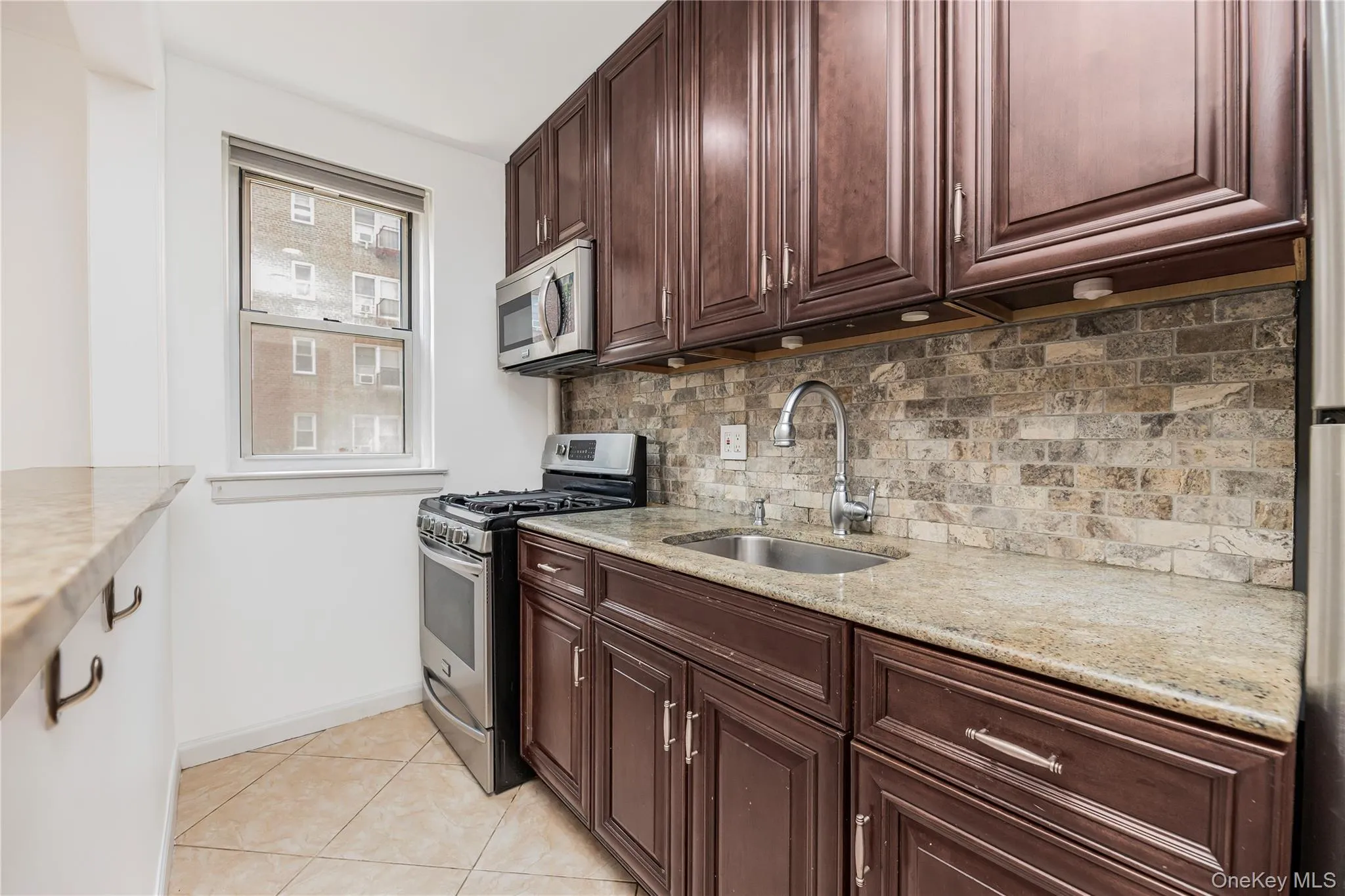 Kitchen with appliances with stainless steel finishes, tasteful backsplash, light tile patterned flooring, light stone counters, and dark brown cabinets Kitchen with appliances with stainless steel finishes, tasteful backsplash, light tile patterned flooring, light stone counters, and dark brown cabinets