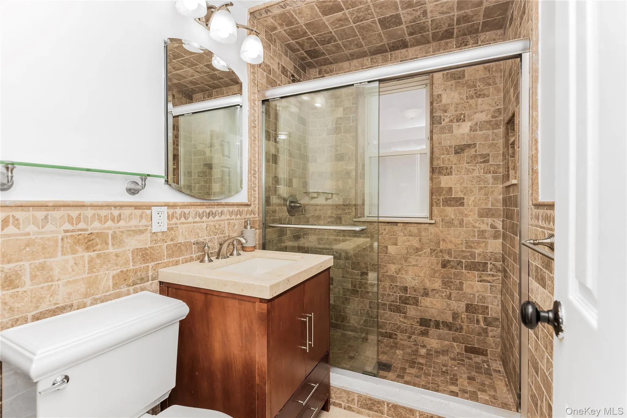 Bathroom featuring vanity, tile walls, wainscoting, and a shower stall Bathroom featuring vanity, tile walls, wainscoting, and a shower stall
