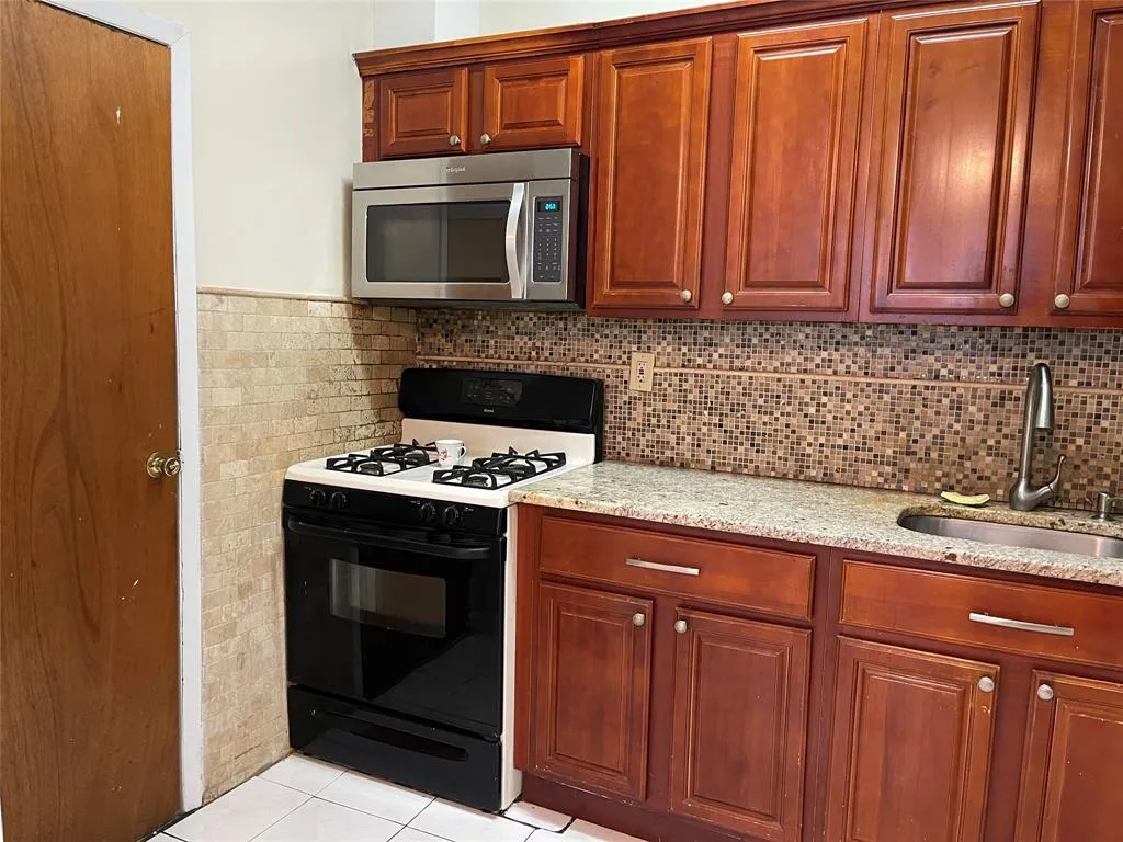Kitchen featuring range with gas stovetop, stainless steel microwave, light stone counters, light tile patterned floors, and decorative backsplash Kitchen featuring range with gas stovetop, stainless steel microwave, light stone counters, light tile patterned floors, and decorative backsplash