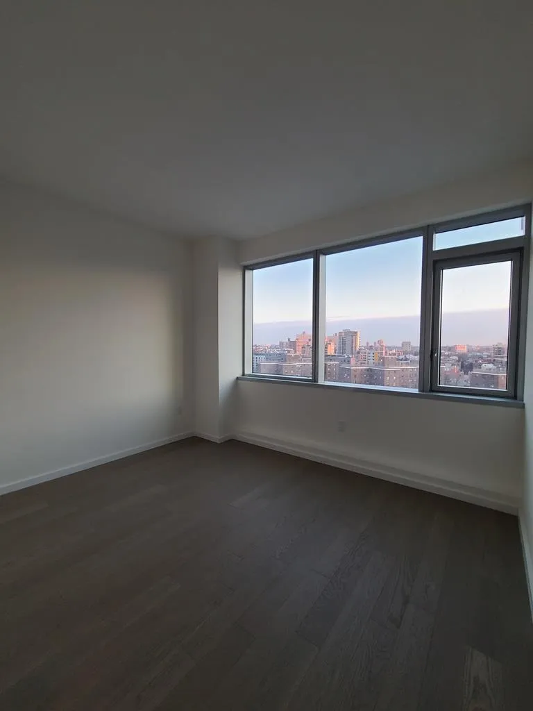 Unfurnished room featuring a view of city and dark wood-type flooring Unfurnished room featuring a view of city and dark wood-type flooring