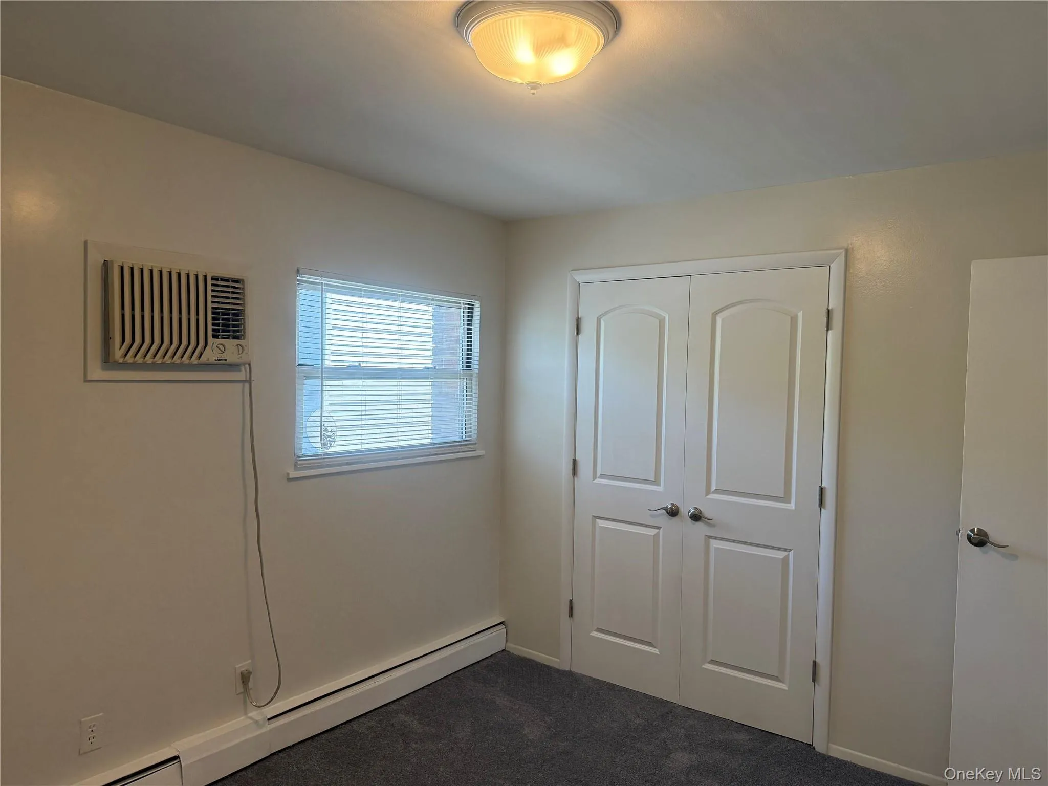 Bedroom featuring new carpet, a large closet, baseboard radiator, and wall mounted AC. Bedroom featuring new carpet, a large closet, baseboard radiator, and wall mounted AC.