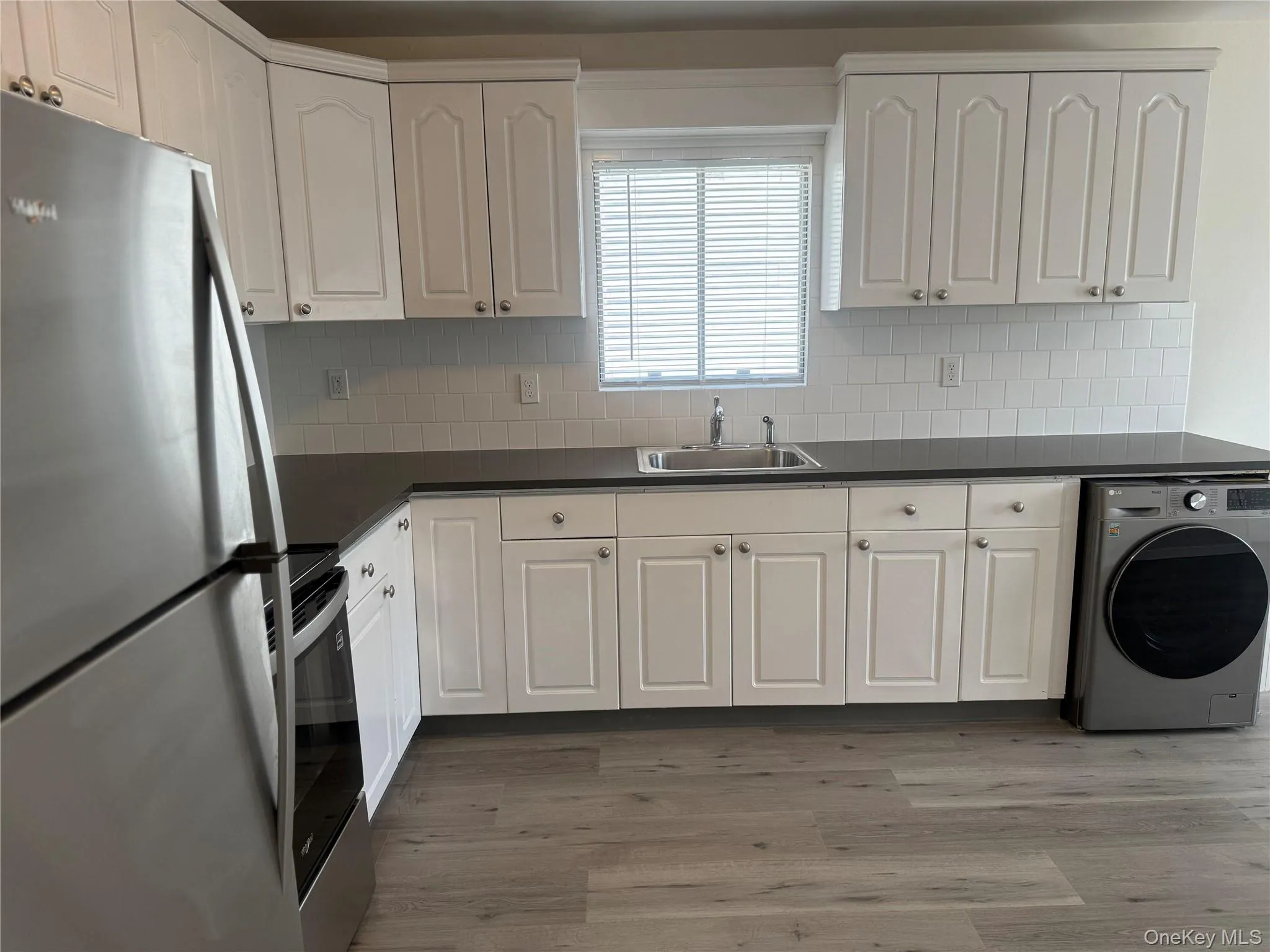 Kitchen featuring stainless steel appliances, combo washer/dryer, light wood-style flooring, dark countertops, and white cabinets. Kitchen featuring stainless steel appliances, combo washer/dryer, light wood-style flooring, dark countertops, and white cabinets.