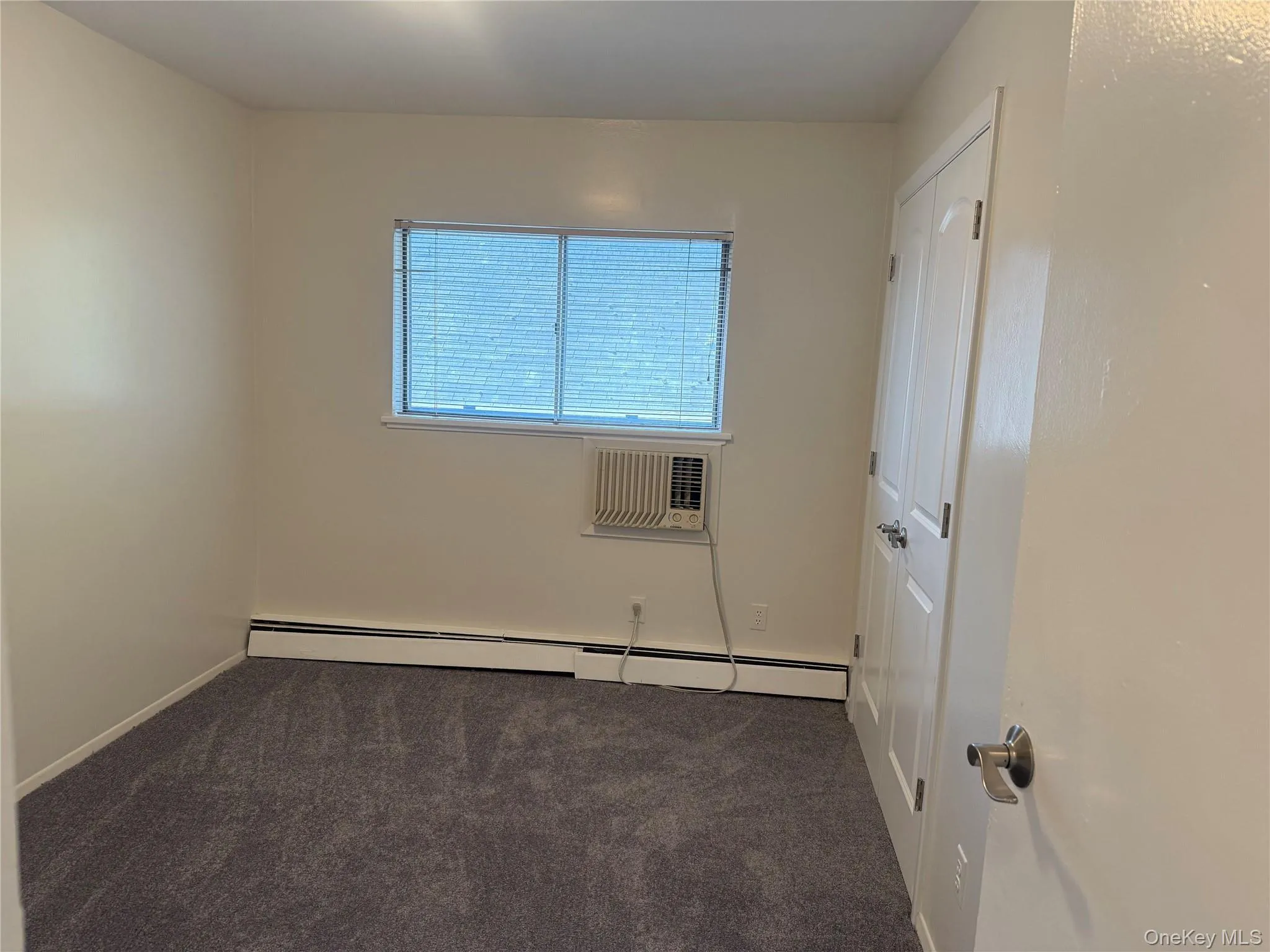 Bedroom featuring new carpet, a large closet, baseboard radiator, and an AC wall unit. Bedroom featuring new carpet, a large closet, baseboard radiator, and an AC wall unit.