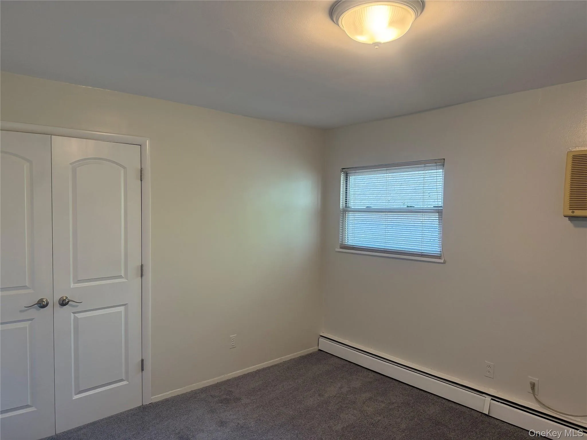 Master bedroom featuring a baseboard radiator, new carpet, large closet, wall unit AC, and master bath. Master bedroom featuring a baseboard radiator, new carpet, large closet, wall unit AC, and master bath.