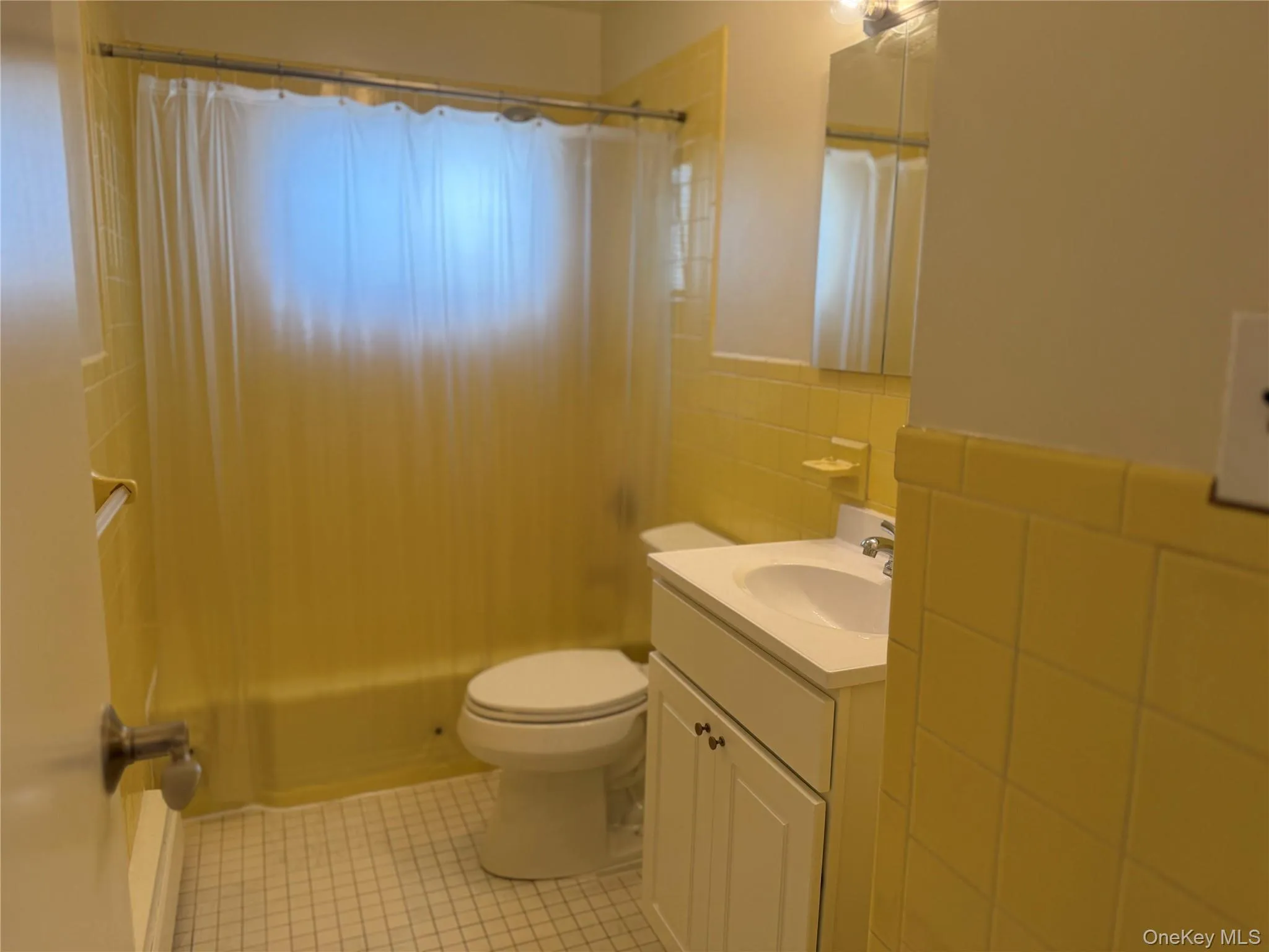 Hall bathroom featuring shower / bath combination with curtain, tile walls, vanity, and light tile patterned floors. Hall bathroom featuring shower / bath combination with curtain, tile walls, vanity, and light tile patterned floors.