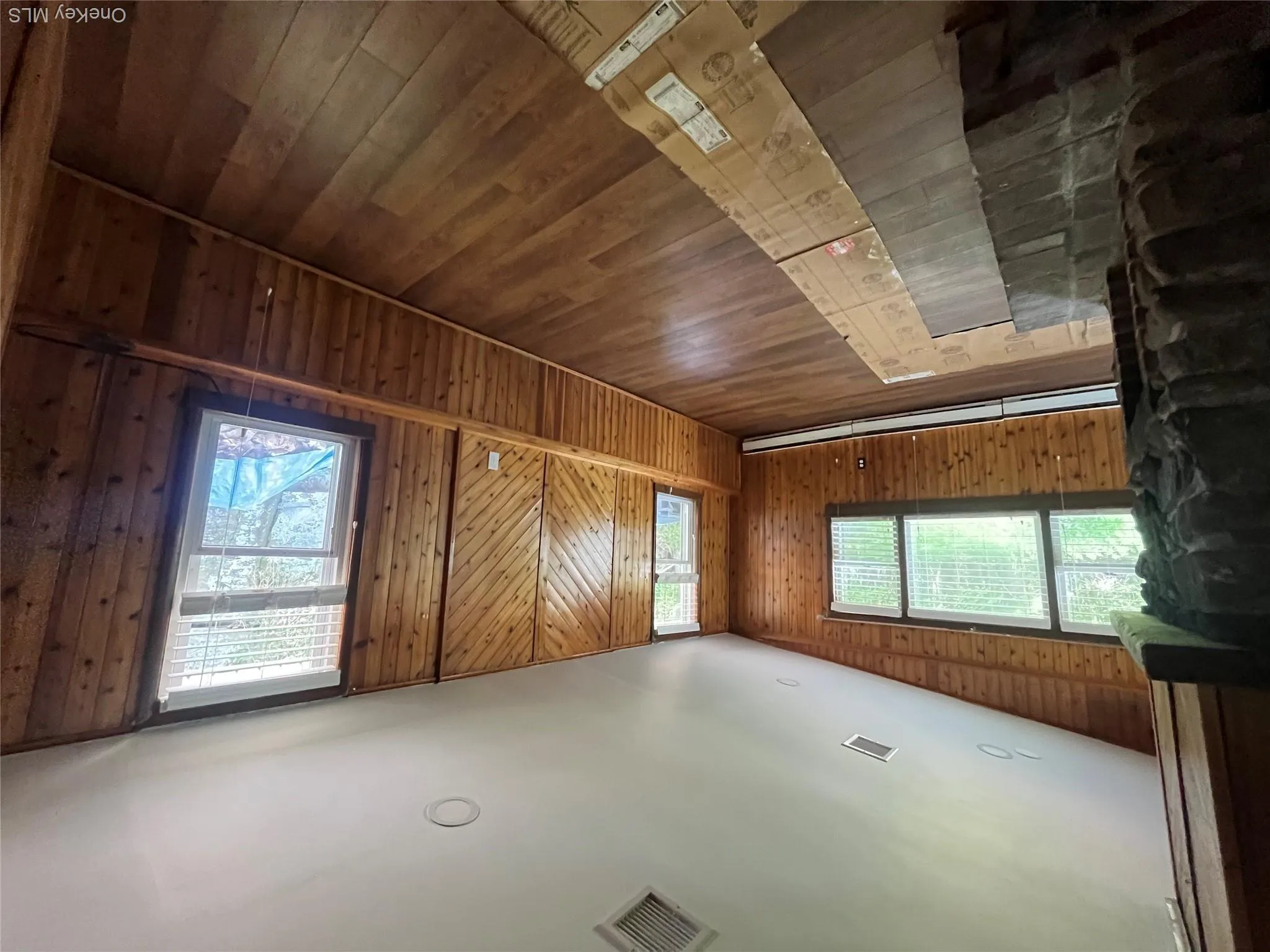 Unfurnished living room featuring wooden walls, wood-type flooring, vaulted ceiling, and a baseboard radiator Unfurnished living room featuring wooden walls, wood-type flooring, vaulted ceiling, and a baseboard radiator