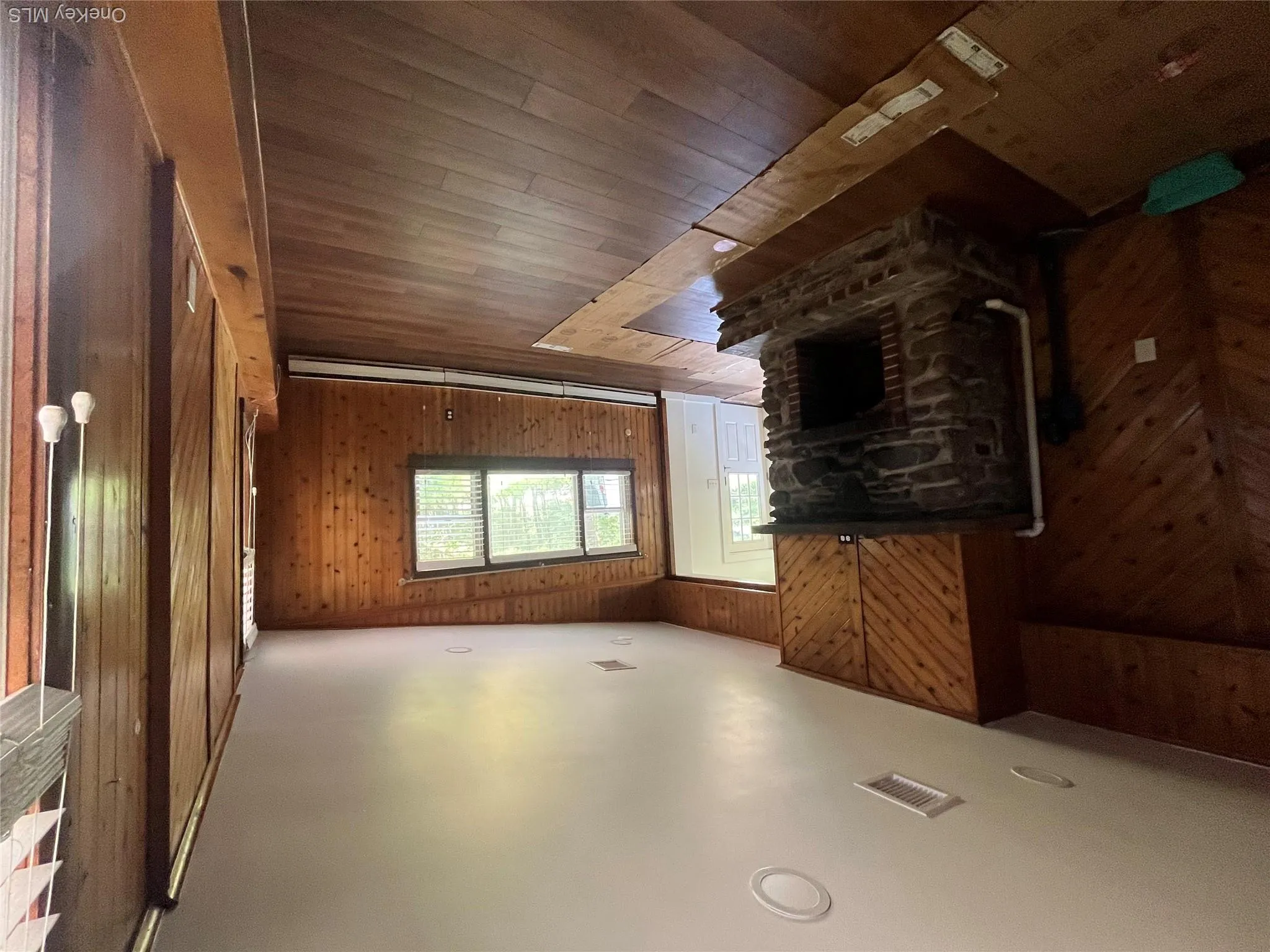 Unfurnished living room with wood walls, a fireplace, hardwood / wood-style flooring, a baseboard heating unit, and lofted ceiling Unfurnished living room with wood walls, a fireplace, hardwood / wood-style flooring, a baseboard heating unit, and lofted ceiling