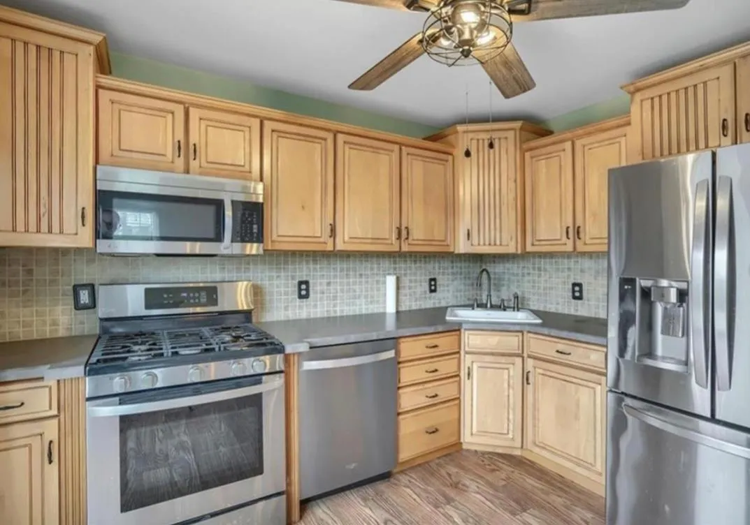 Kitchen with stainless steel appliances, light wood finished floors, light brown cabinets, ceiling fan, and tasteful backsplash Kitchen with stainless steel appliances, light wood finished floors, light brown cabinets, ceiling fan, and tasteful backsplash
