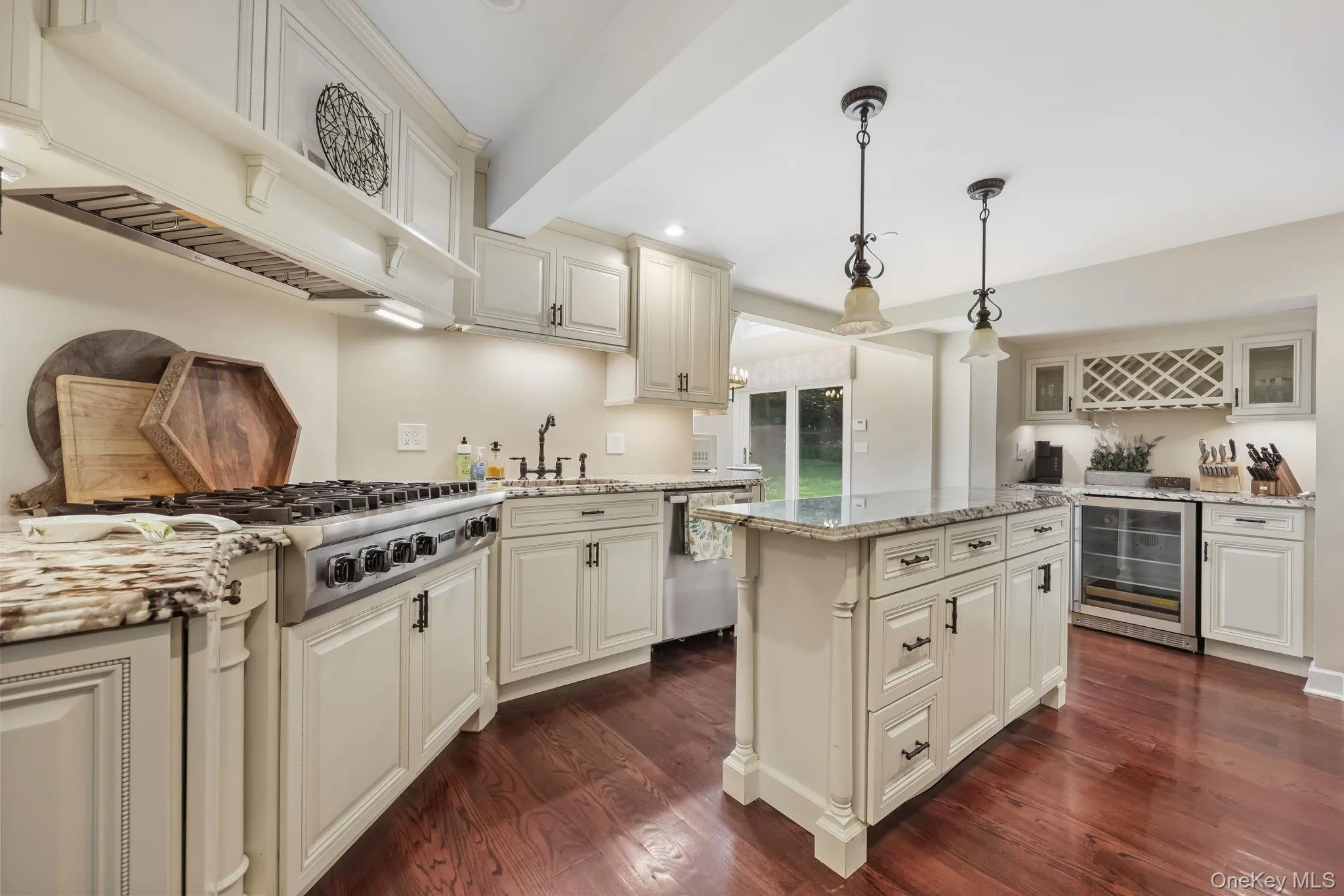 Kitchen with decorative light fixtures, light stone countertops, dark wood finished floors, premium range hood, and wine cooler Kitchen with decorative light fixtures, light stone countertops, dark wood finished floors, premium range hood, and wine cooler