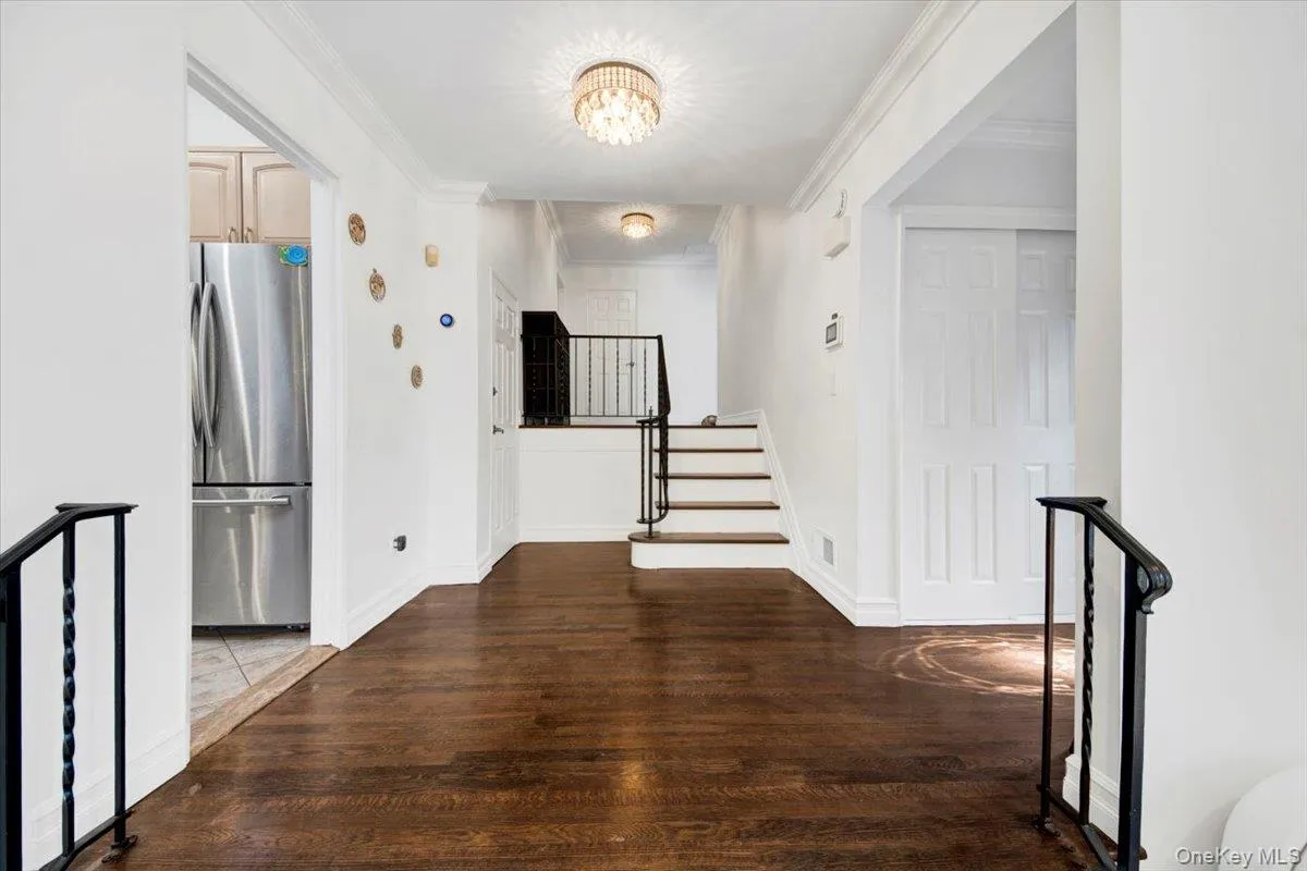 Hallway with stairway, crown molding, wood finished floors, a chandelier, and an upstairs landing Hallway with stairway, crown molding, wood finished floors, a chandelier, and an upstairs landing