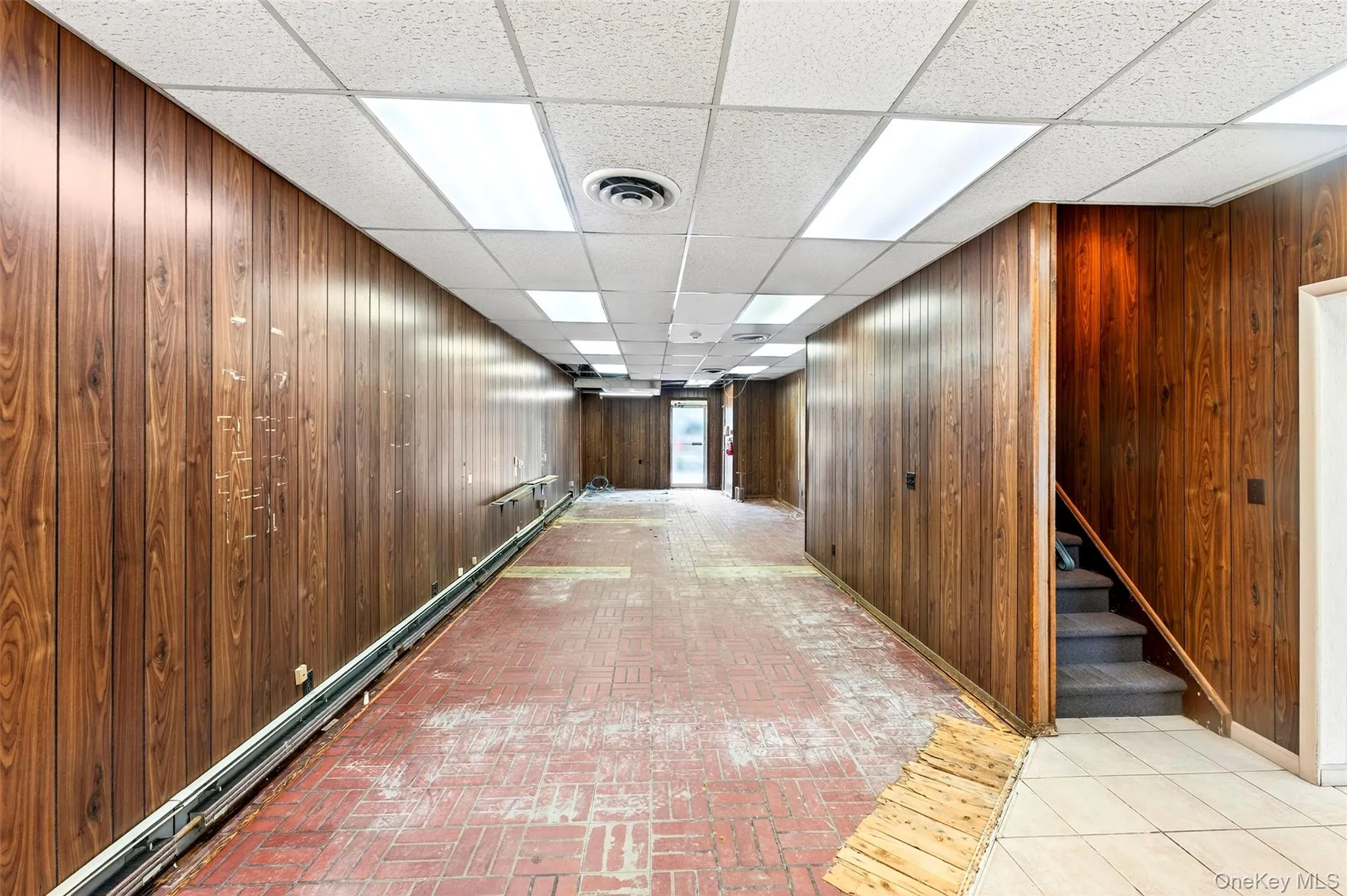 Hall with a paneled ceiling, wooden walls, stairs, baseboard heating, and brick patterned floors Hall with a paneled ceiling, wooden walls, stairs, baseboard heating, and brick patterned floors