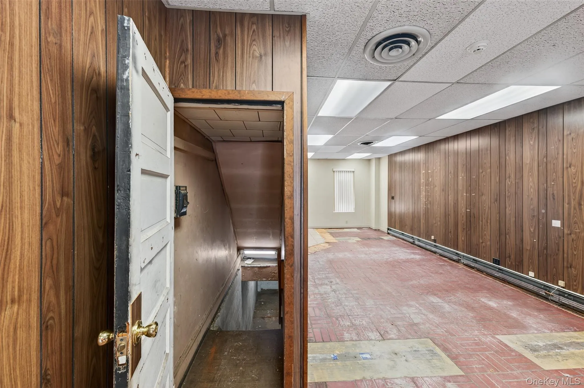 Hallway with wood walls, a paneled ceiling, and a baseboard heating unit Hallway with wood walls, a paneled ceiling, and a baseboard heating unit