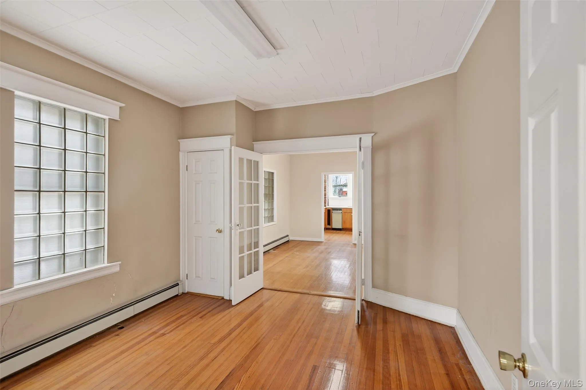 Unfurnished bedroom featuring baseboard heating, light wood-type flooring, and crown molding Unfurnished bedroom featuring baseboard heating, light wood-type flooring, and crown molding