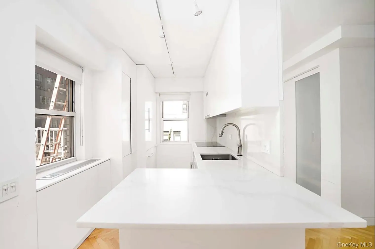 Kitchen with white cabinetry, rail lighting, a peninsula, modern cabinets, and light stone countertops Kitchen with white cabinetry, rail lighting, a peninsula, modern cabinets, and light stone countertops