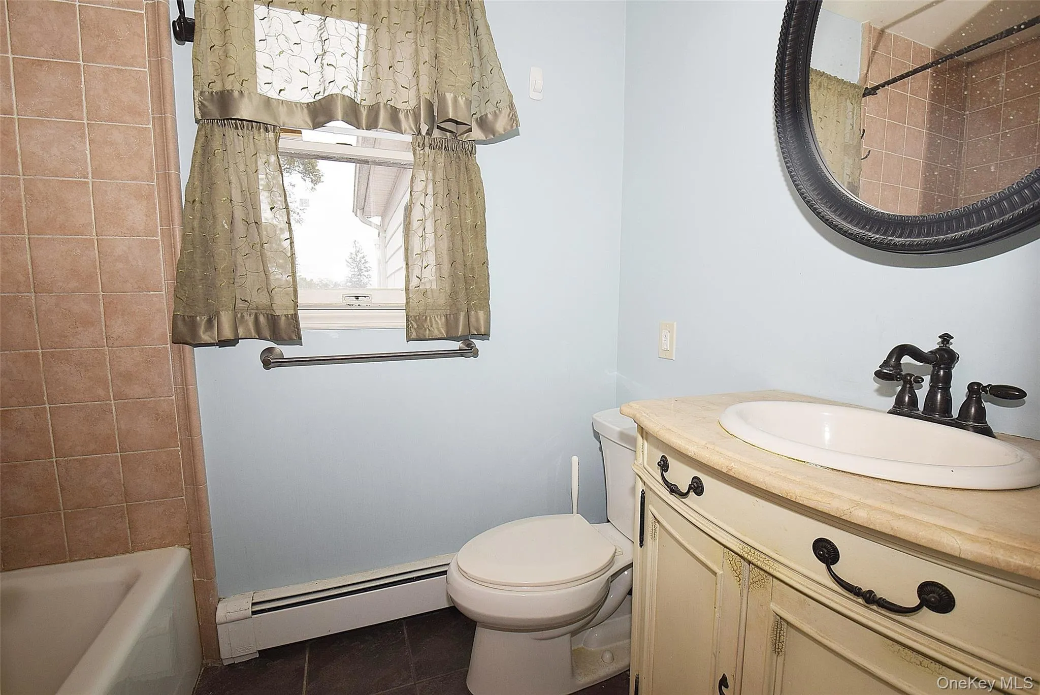 Full bath with a baseboard heating unit, vanity, dark tile patterned flooring, and washtub / shower combination Full bath with a baseboard heating unit, vanity, dark tile patterned flooring, and washtub / shower combination