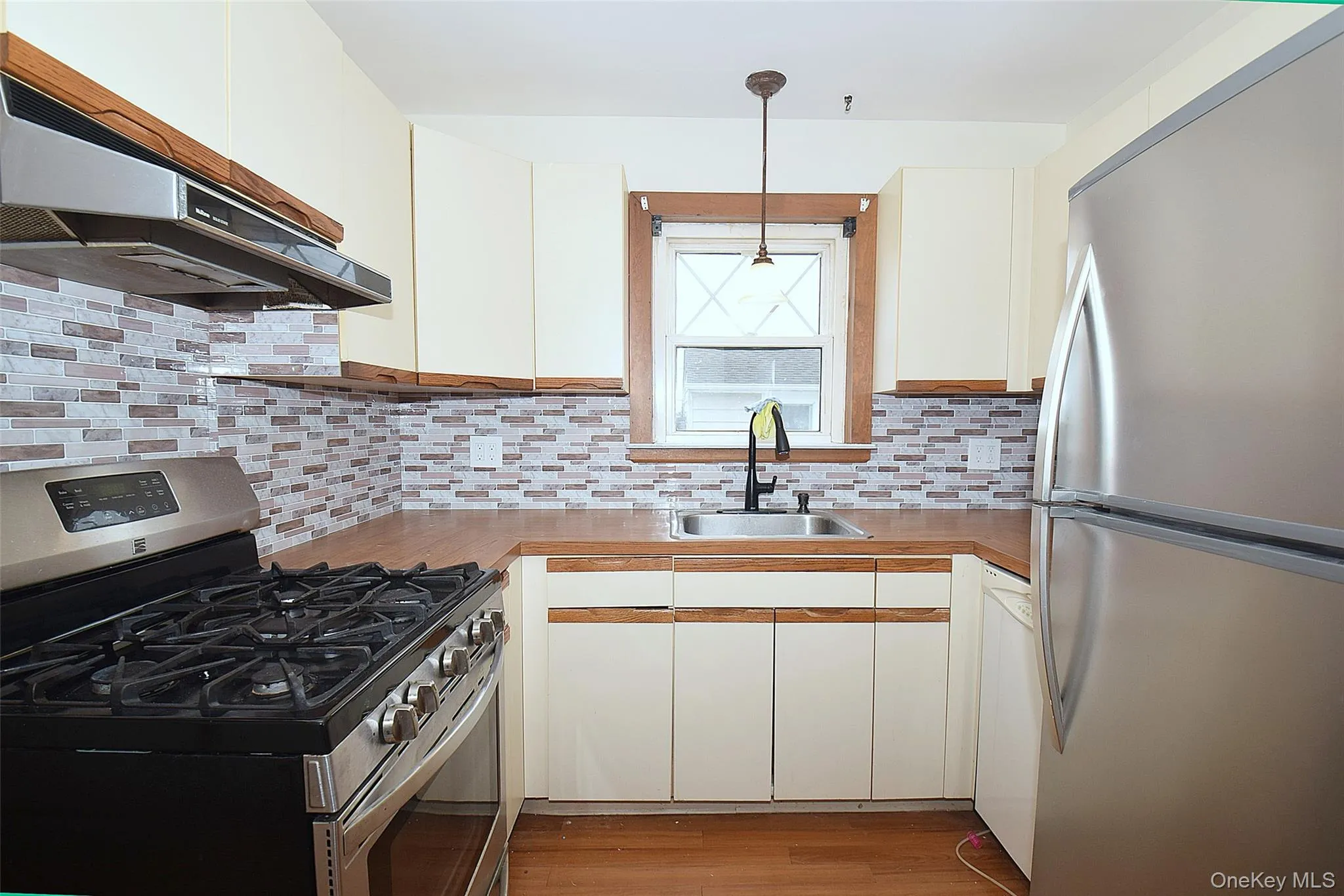 Kitchen featuring stainless steel appliances, white cabinetry, light countertops, backsplash, and under cabinet range hood Kitchen featuring stainless steel appliances, white cabinetry, light countertops, backsplash, and under cabinet range hood