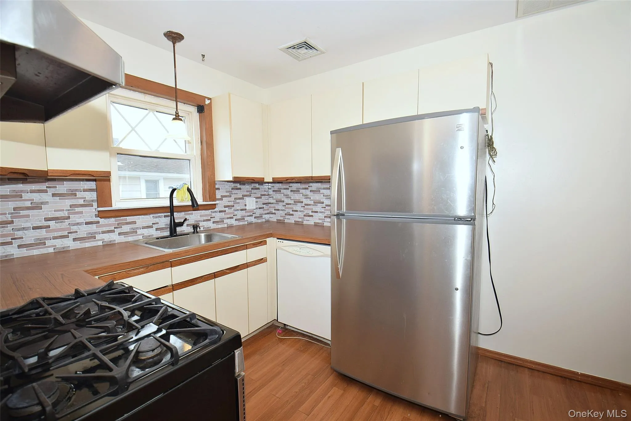 Kitchen featuring under cabinet range hood, black gas range, freestanding refrigerator, wood finished floors, and dishwasher Kitchen featuring under cabinet range hood, black gas range, freestanding refrigerator, wood finished floors, and dishwasher