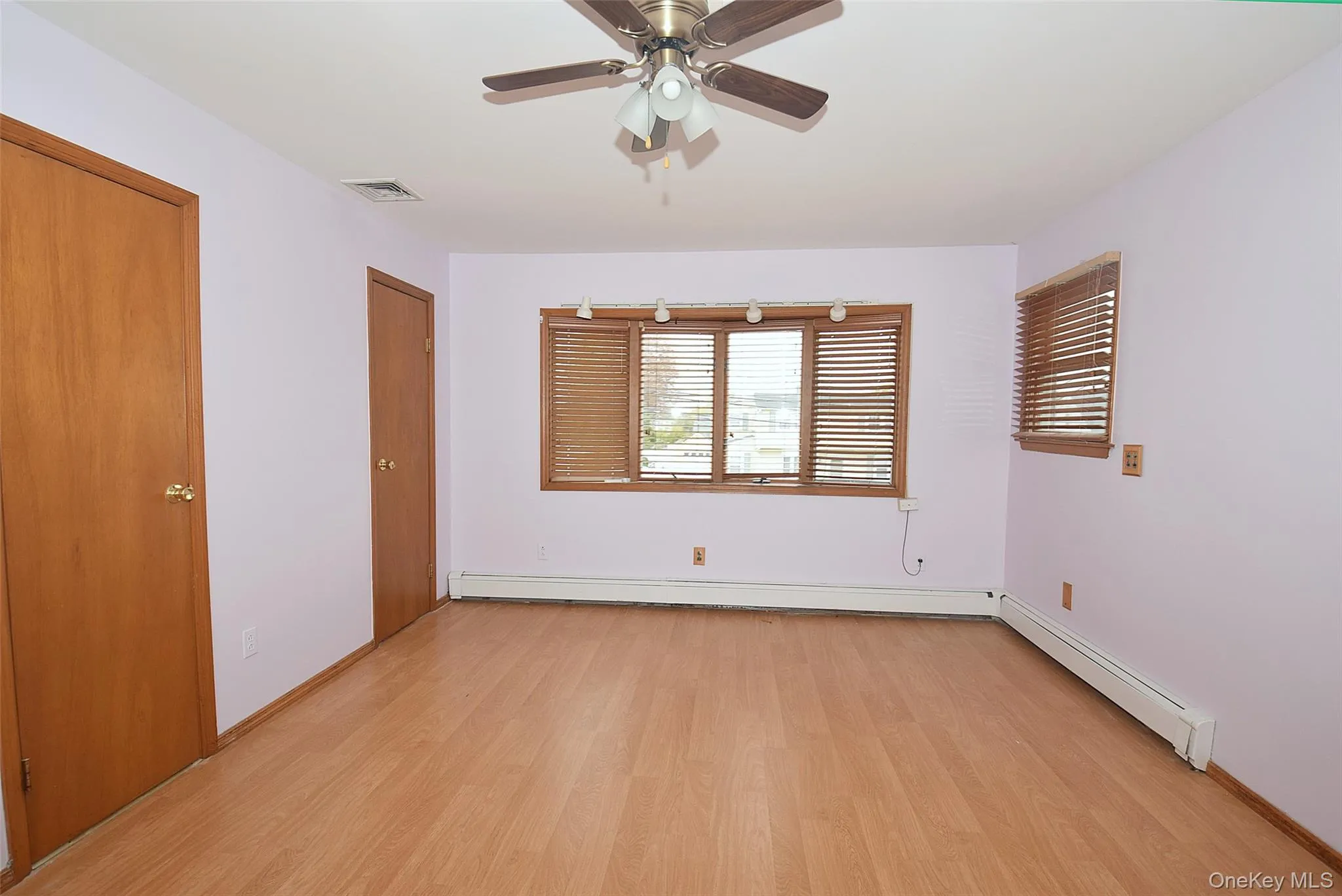 Unfurnished bedroom with light wood-type flooring, a ceiling fan, and a baseboard heating unit Unfurnished bedroom with light wood-type flooring, a ceiling fan, and a baseboard heating unit