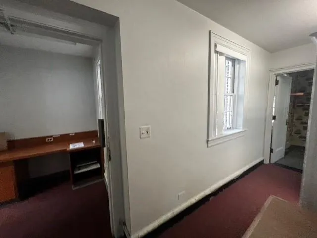 Hallway featuring dark carpet and baseboards Hallway featuring dark carpet and baseboards