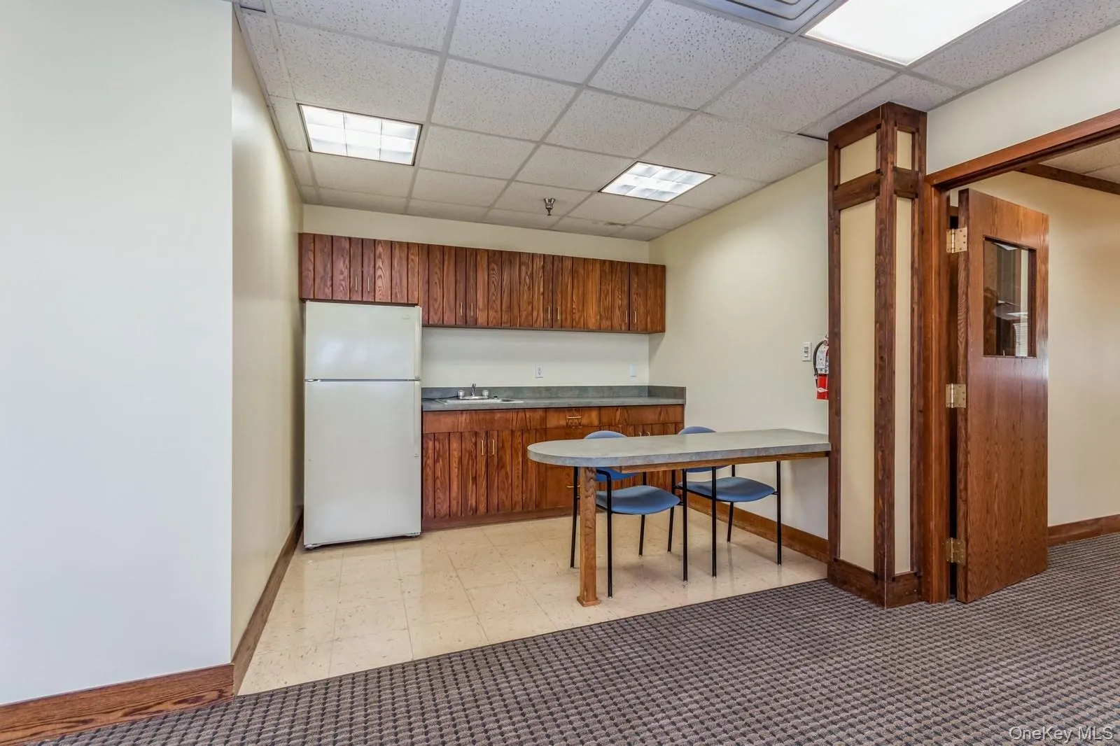 Kitchen with a drop ceiling, freestanding refrigerator, light flooring, and brown cabinets Kitchen with a drop ceiling, freestanding refrigerator, light flooring, and brown cabinets