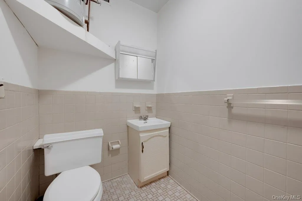 Half bathroom featuring vanity, tile patterned floors, a wainscoted wall, and tile walls Half bathroom featuring vanity, tile patterned floors, a wainscoted wall, and tile walls