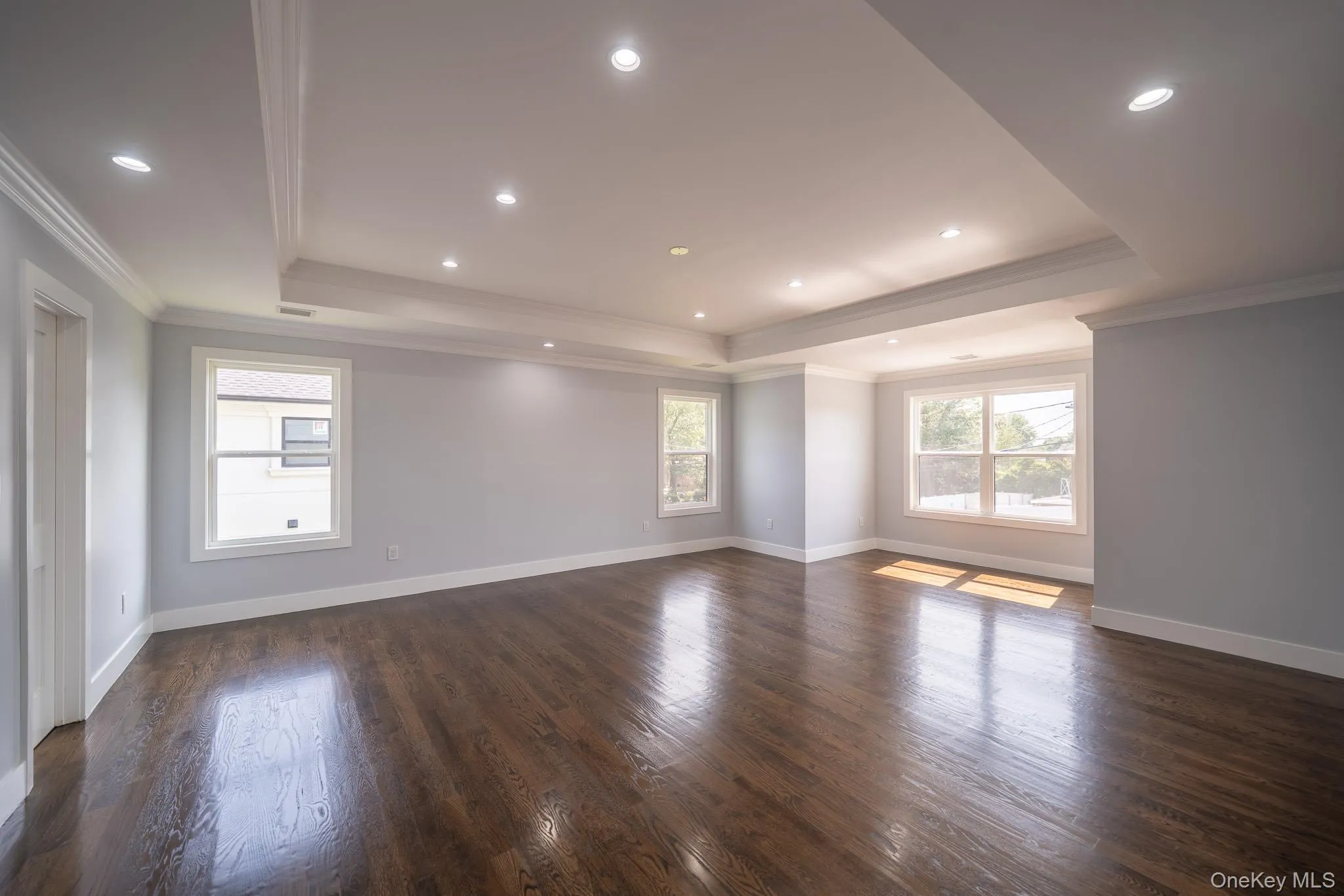 Empty room with ornamental molding, a tray ceiling, dark wood-style flooring, and recessed lighting Empty room with ornamental molding, a tray ceiling, dark wood-style flooring, and recessed lighting