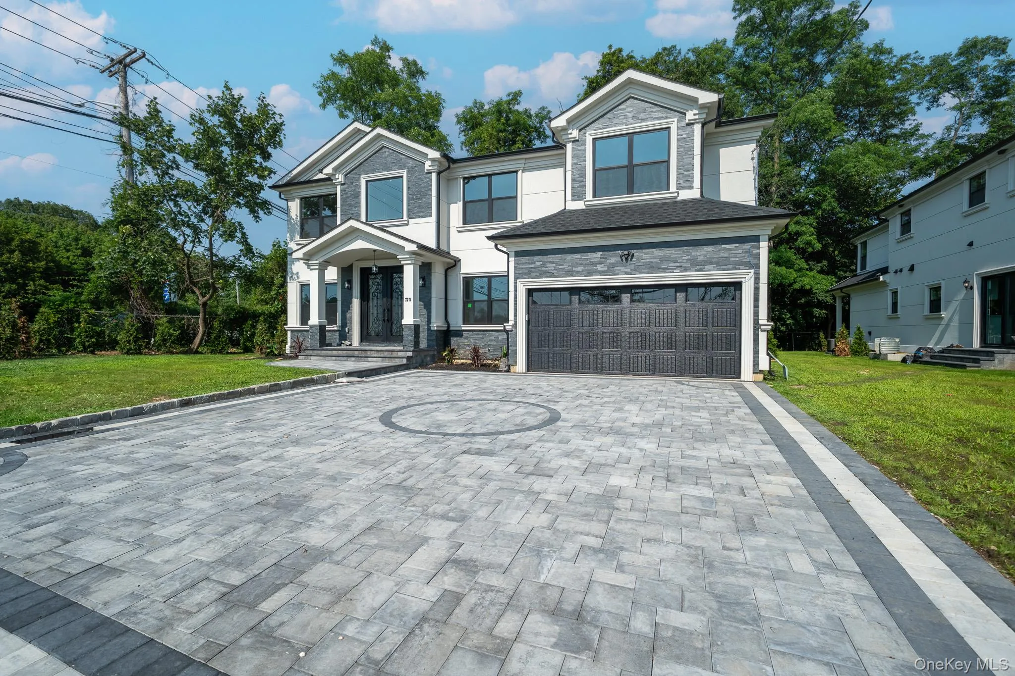 View of front facade with decorative driveway, a garage, a front yard, and stone siding View of front facade with decorative driveway, a garage, a front yard, and stone siding