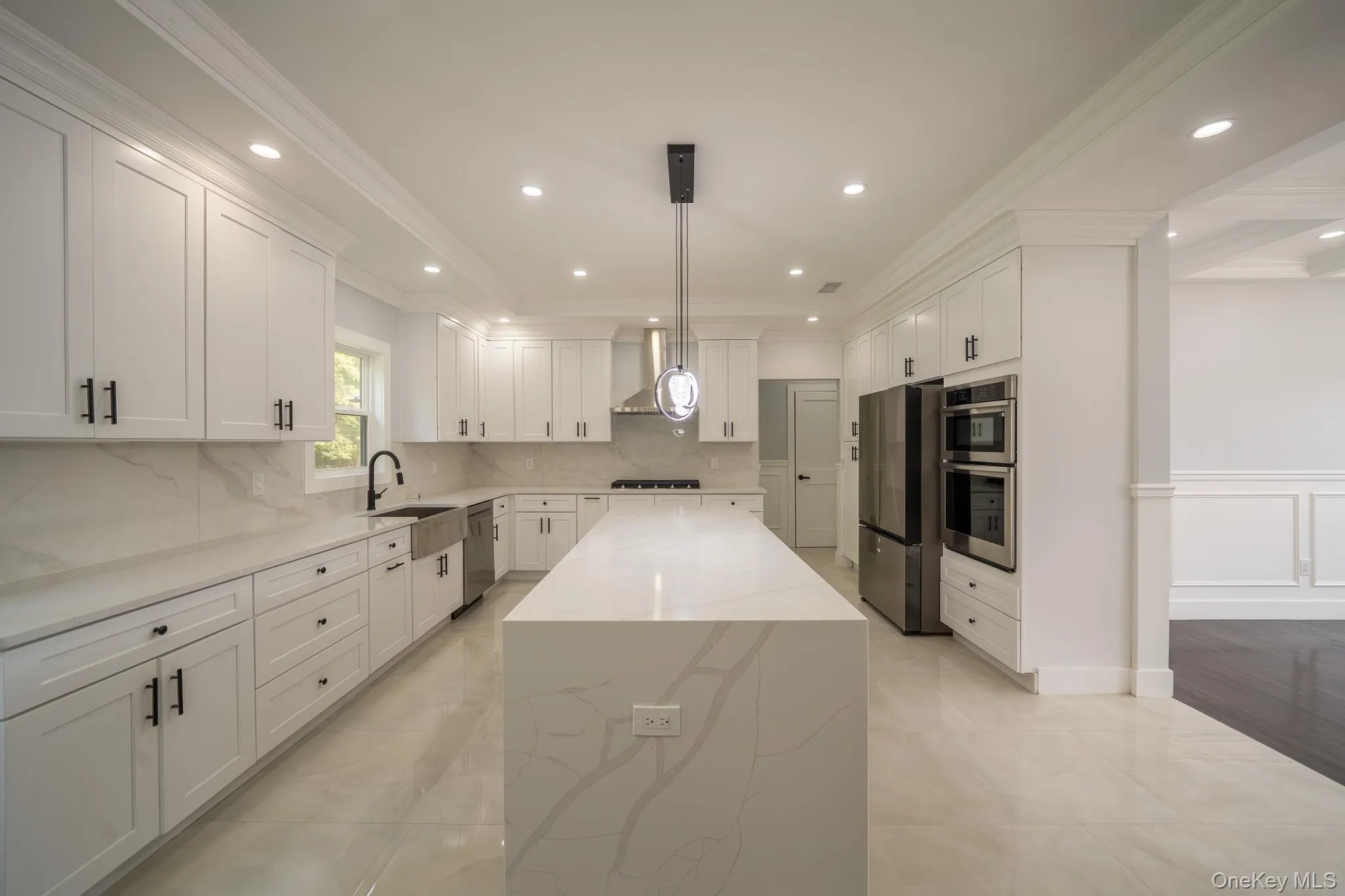 Kitchen featuring ornamental molding, backsplash, white cabinetry, light stone countertops, and a center island Kitchen featuring ornamental molding, backsplash, white cabinetry, light stone countertops, and a center island