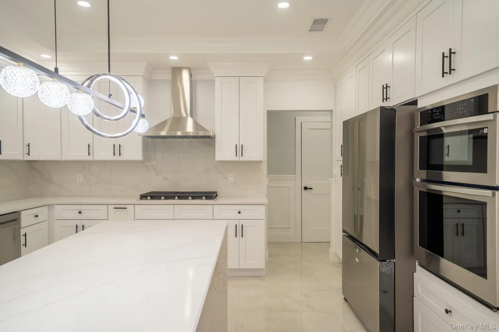 Kitchen featuring stainless steel appliances, decorative backsplash, crown molding, white cabinetry, and wall chimney exhaust hood Kitchen featuring stainless steel appliances, decorative backsplash, crown molding, white cabinetry, and wall chimney exhaust hood