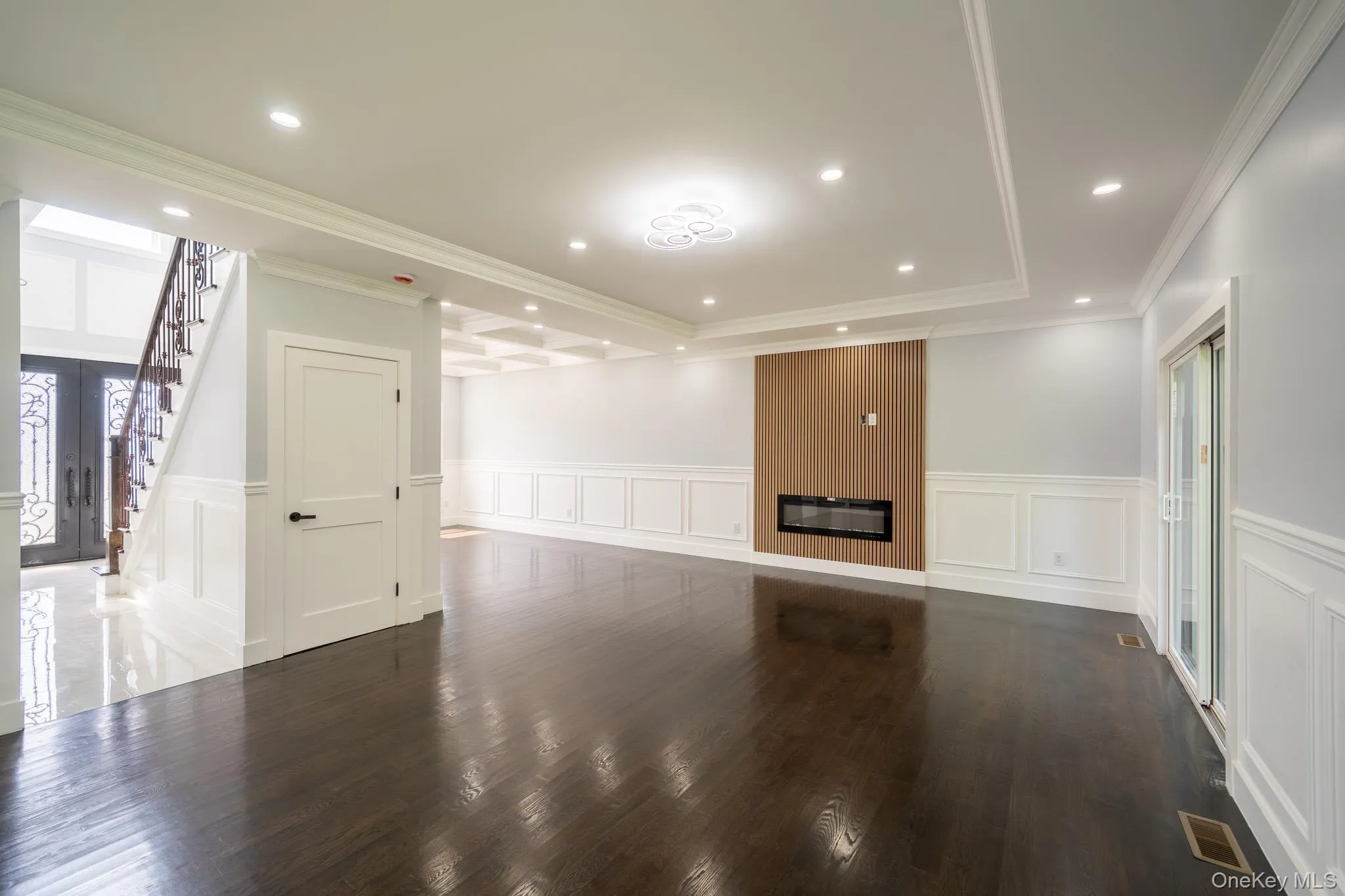 Unfurnished living room with wainscoting, a decorative wall, ornamental molding, dark wood-type flooring, and stairway Unfurnished living room with wainscoting, a decorative wall, ornamental molding, dark wood-type flooring, and stairway