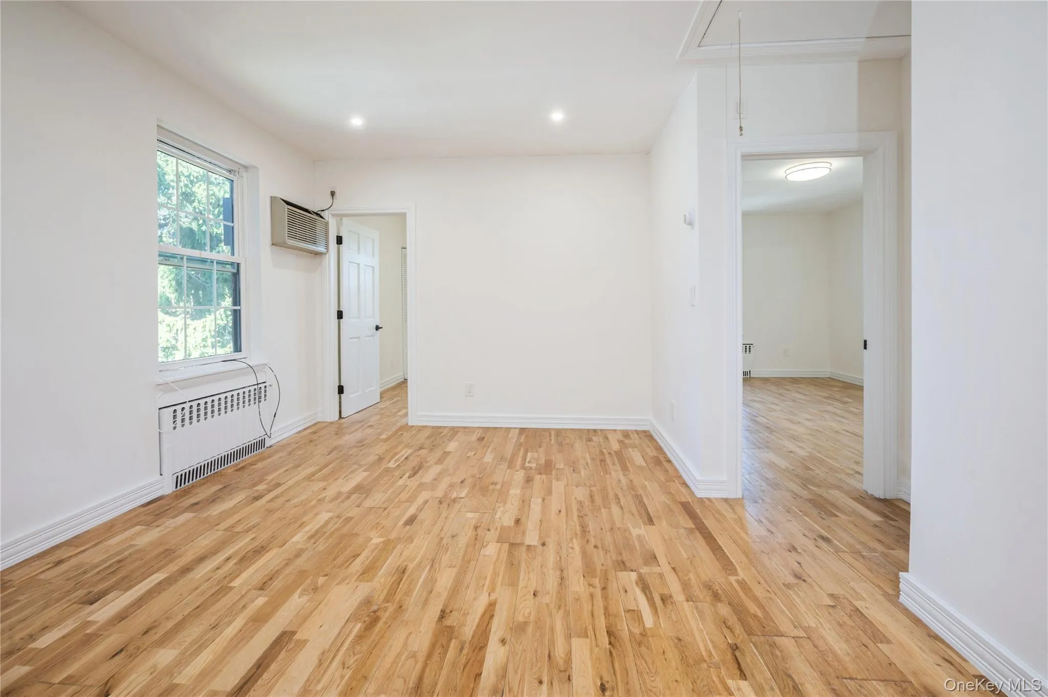 Unfurnished room with light wood-style flooring, radiator heating unit, attic access, recessed lighting, and a wall mounted AC Unfurnished room with light wood-style flooring, radiator heating unit, attic access, recessed lighting, and a wall mounted AC