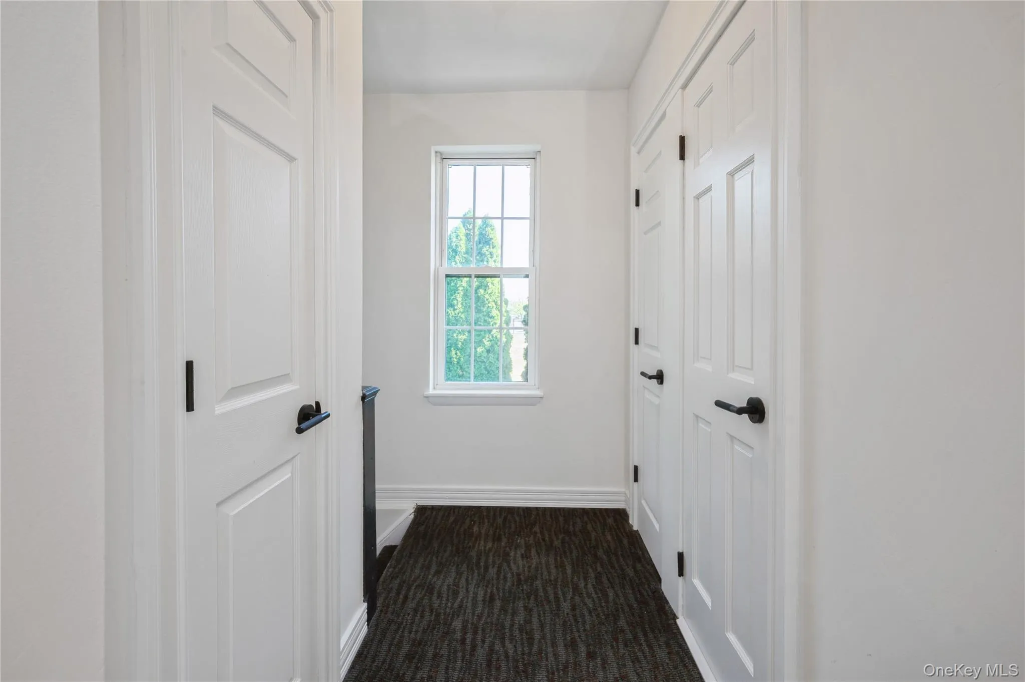 Hallway featuring baseboards and dark colored carpet Hallway featuring baseboards and dark colored carpet