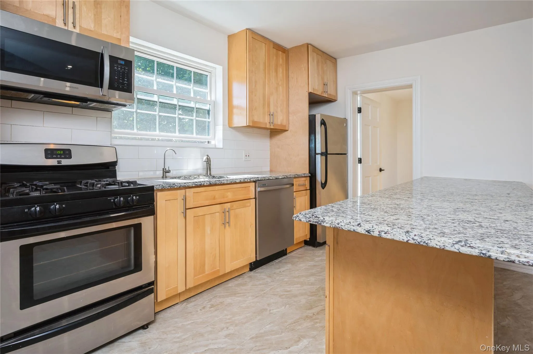 Kitchen featuring appliances with stainless steel finishes, backsplash, light stone countertops, and light brown cabinets Kitchen featuring appliances with stainless steel finishes, backsplash, light stone countertops, and light brown cabinets