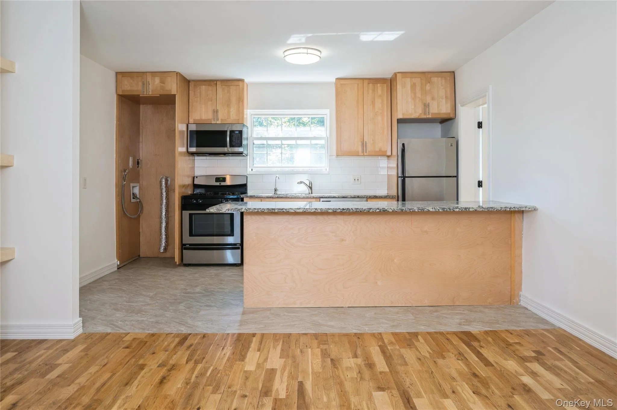 Kitchen featuring tasteful backsplash, appliances with stainless steel finishes, light wood-style flooring, light stone countertops, and a peninsula Kitchen featuring tasteful backsplash, appliances with stainless steel finishes, light wood-style flooring, light stone countertops, and a peninsula
