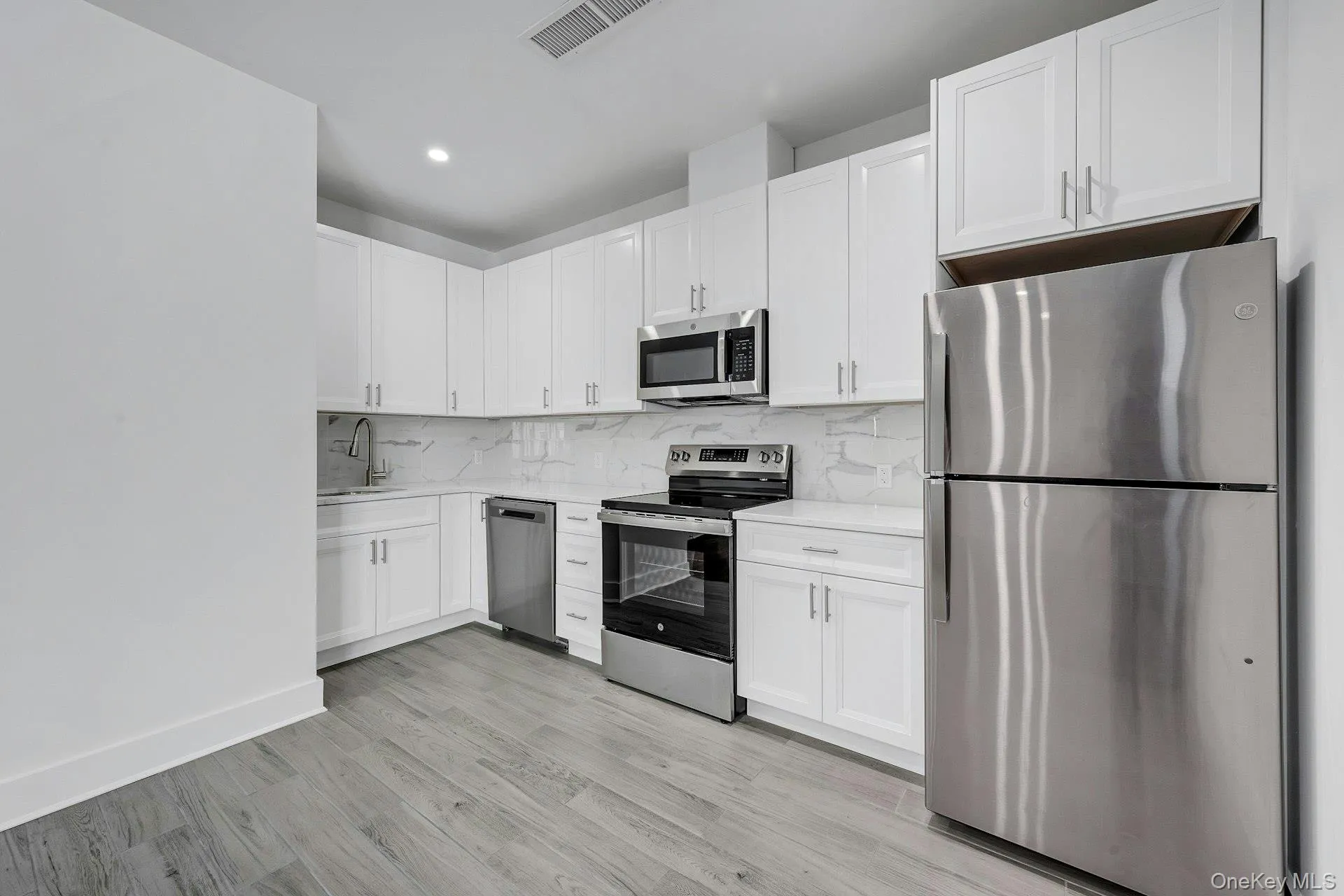 Kitchen with appliances with stainless steel finishes, backsplash, white cabinets, light wood finished floors, and light stone countertops Kitchen with appliances with stainless steel finishes, backsplash, white cabinets, light wood finished floors, and light stone countertops
