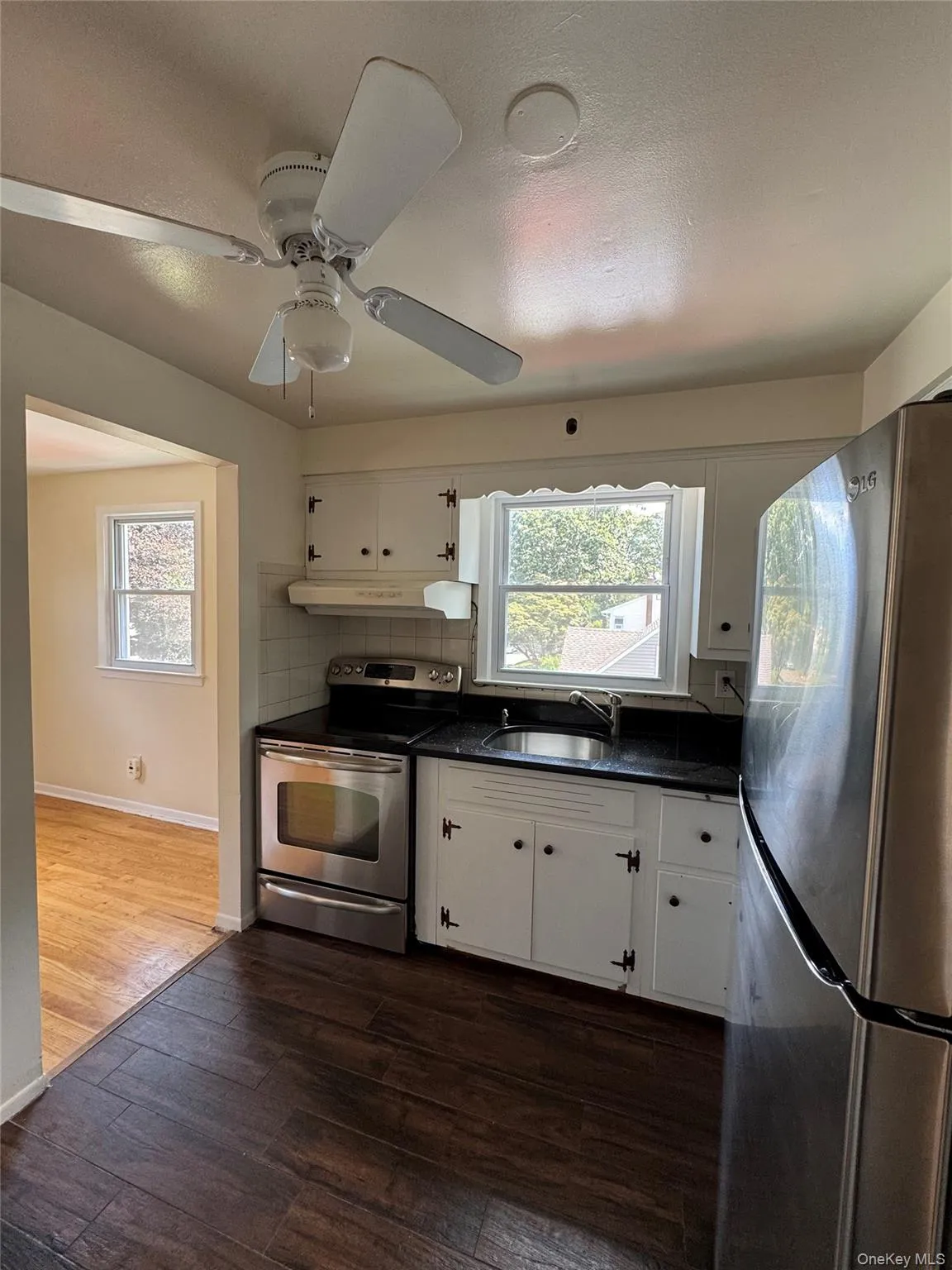 Kitchen with stainless steel appliances, white cabinetry, backsplash, dark wood finished floors, and a textured ceiling Kitchen with stainless steel appliances, white cabinetry, backsplash, dark wood finished floors, and a textured ceiling