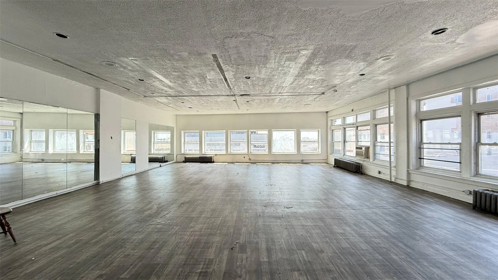 Unfurnished living room with plenty of natural light, wood finished floors, a textured ceiling, and radiator Unfurnished living room with plenty of natural light, wood finished floors, a textured ceiling, and radiator