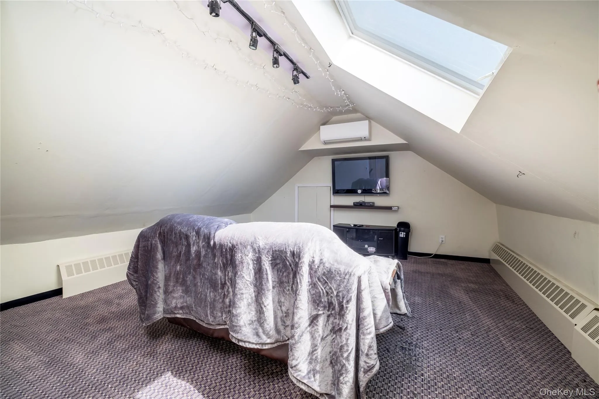 Bedroom with a skylight, carpet floors, vaulted ceiling, track lighting, and a wall mounted AC Bedroom with a skylight, carpet floors, vaulted ceiling, track lighting, and a wall mounted AC