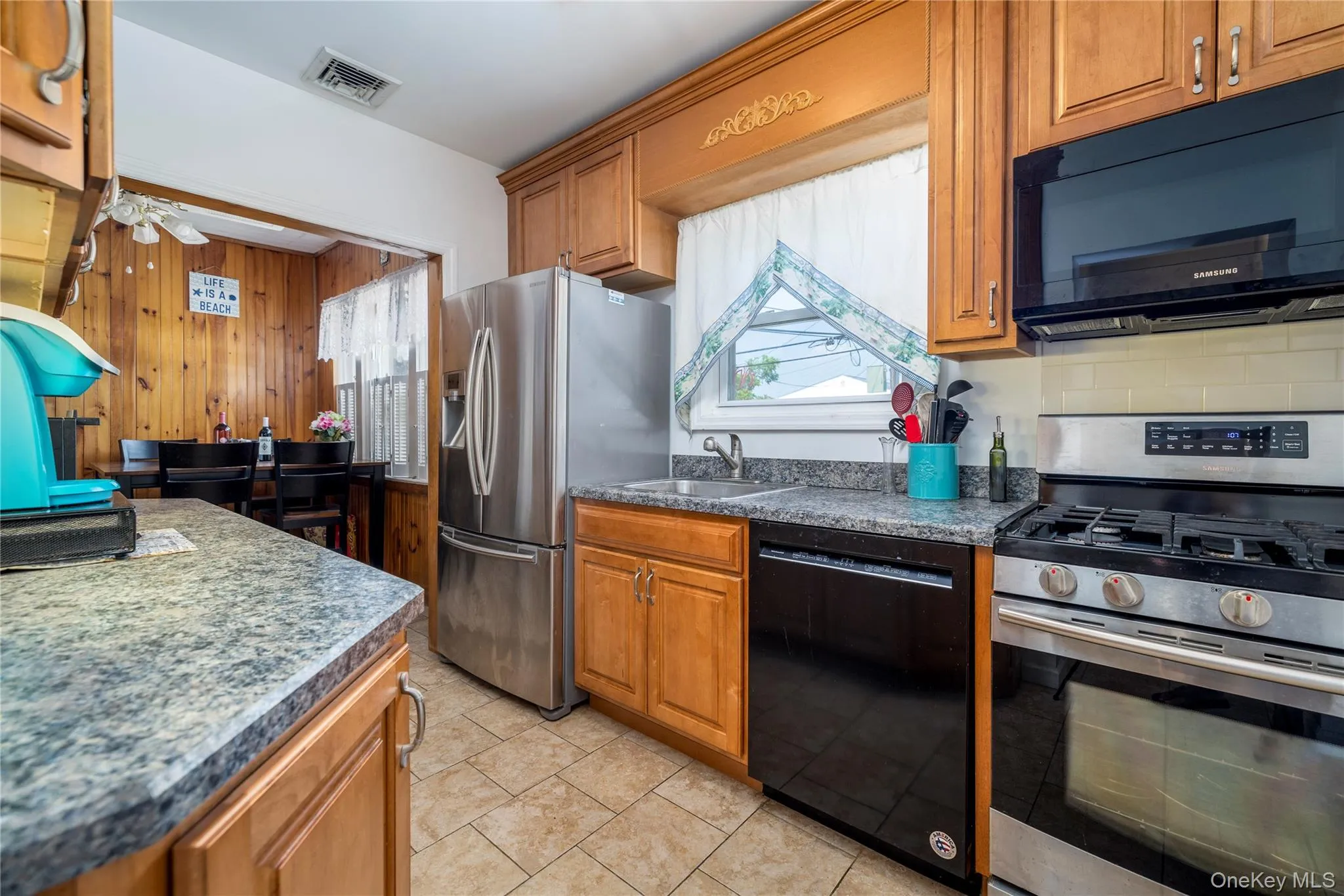 Kitchen with black appliances, brown cabinetry, dark countertops, and light tile patterned floors Kitchen with black appliances, brown cabinetry, dark countertops, and light tile patterned floors