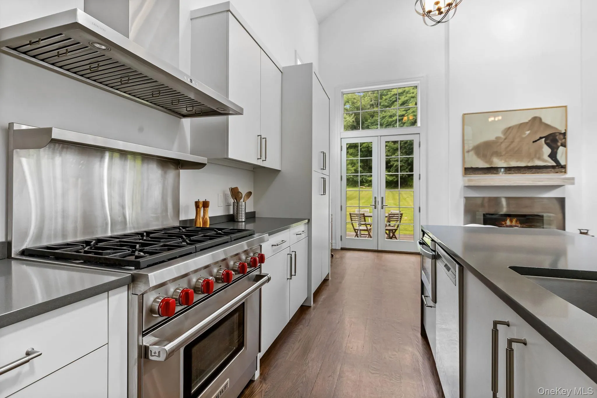 Open Kitchen featuring stainless steel appliances, wall range hood, dark countertops, wood flooring, and white cabinetry Open Kitchen featuring stainless steel appliances, wall range hood, dark countertops, wood flooring, and white cabinetry