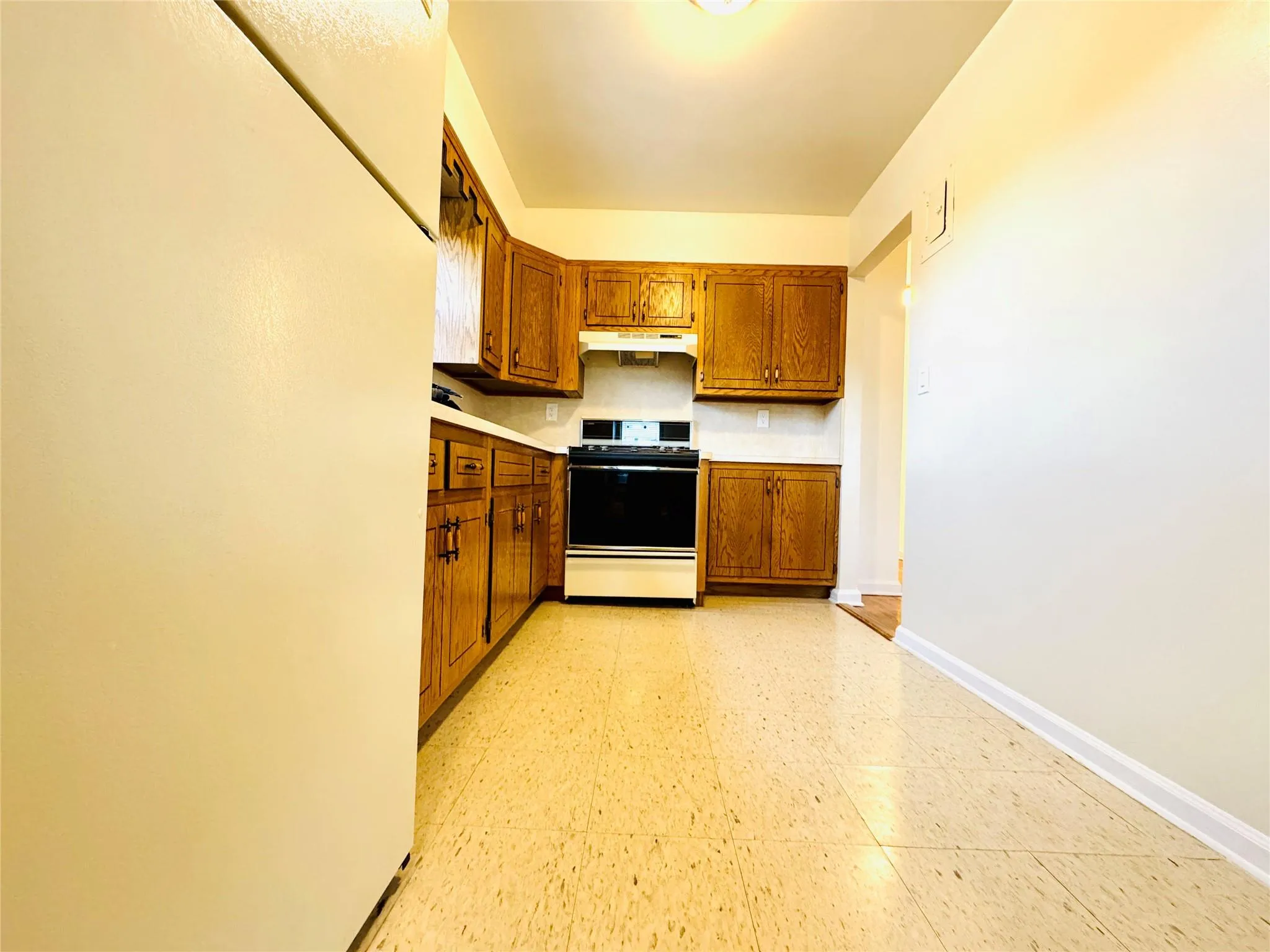 Kitchen with brown cabinetry, light floors, range, light countertops, and under cabinet range hood Kitchen with brown cabinetry, light floors, range, light countertops, and under cabinet range hood