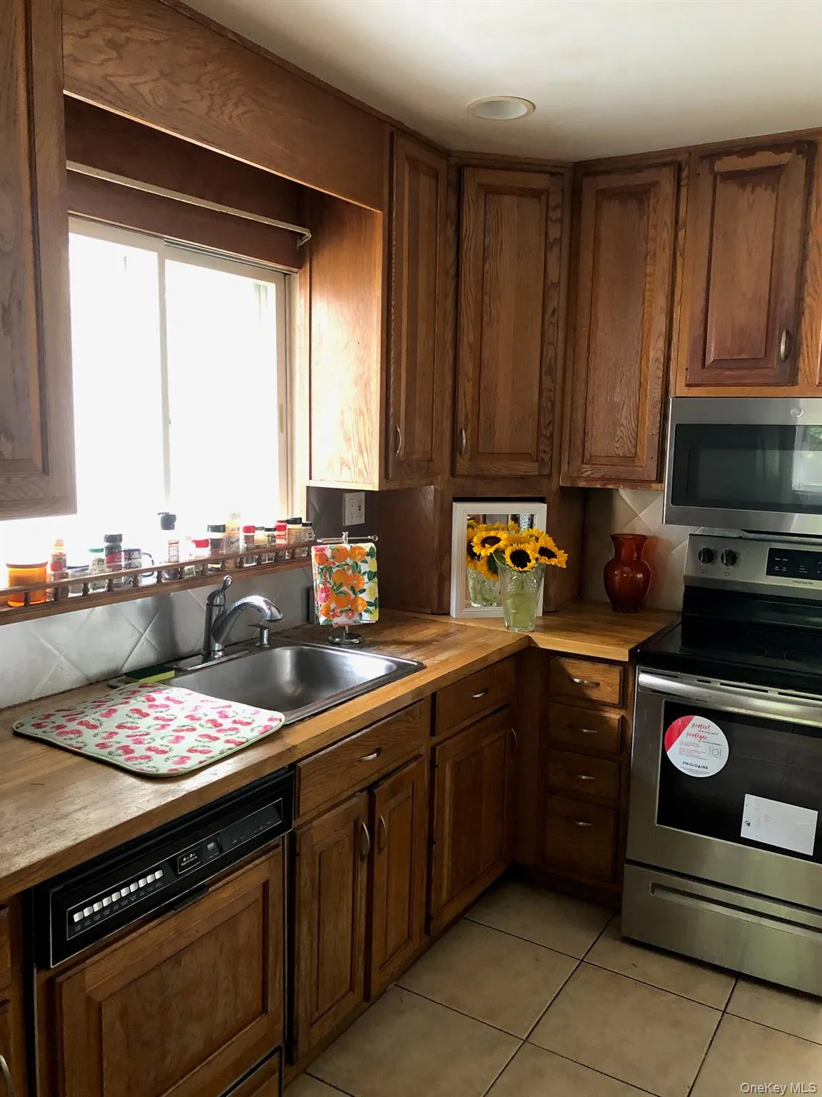 Kitchen featuring stainless steel appliances, light tile patterned floors, butcher block countertops, tasteful backsplash, and dark brown cabinets Kitchen featuring stainless steel appliances, light tile patterned floors, butcher block countertops, tasteful backsplash, and dark brown cabinets