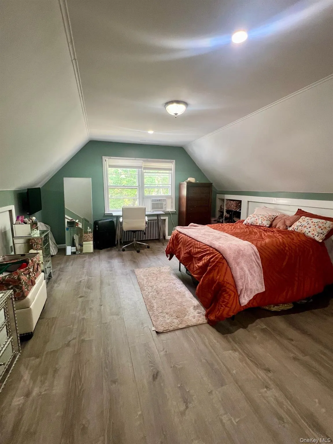 Bedroom featuring vaulted ceiling, wood finished floors, and radiator heating unit Bedroom featuring vaulted ceiling, wood finished floors, and radiator heating unit