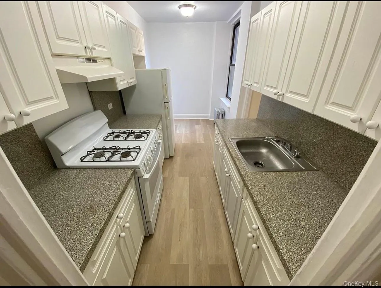 Kitchen featuring light wood-style flooring, gas range gas stove, white cabinetry, under cabinet range hood, and dark countertops Kitchen featuring light wood-style flooring, gas range gas stove, white cabinetry, under cabinet range hood, and dark countertops