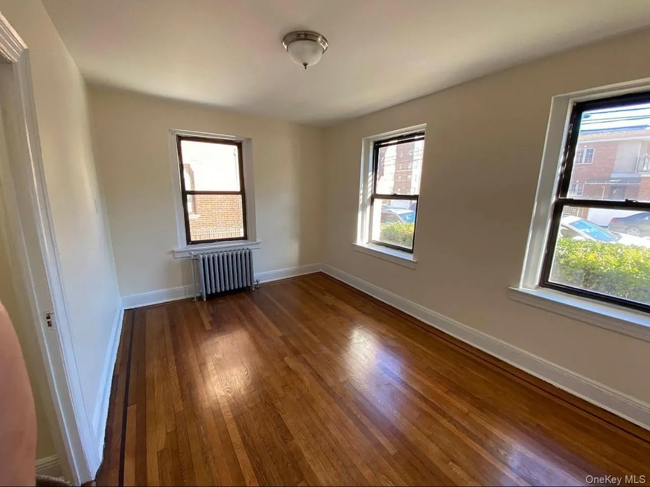 Unfurnished room with dark wood-type flooring, radiator heating unit, and healthy amount of natural light Unfurnished room with dark wood-type flooring, radiator heating unit, and healthy amount of natural light