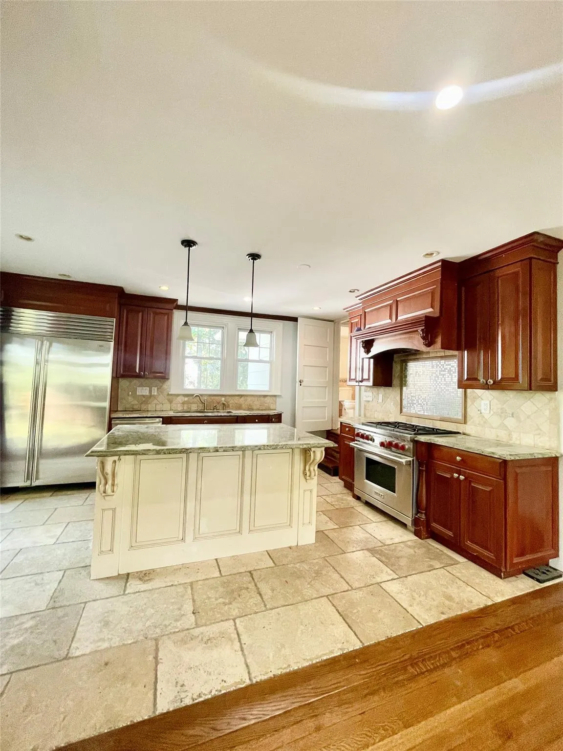 Kitchen with decorative backsplash, premium appliances, stone tile floors, light stone counters, and a center island Kitchen with decorative backsplash, premium appliances, stone tile floors, light stone counters, and a center island